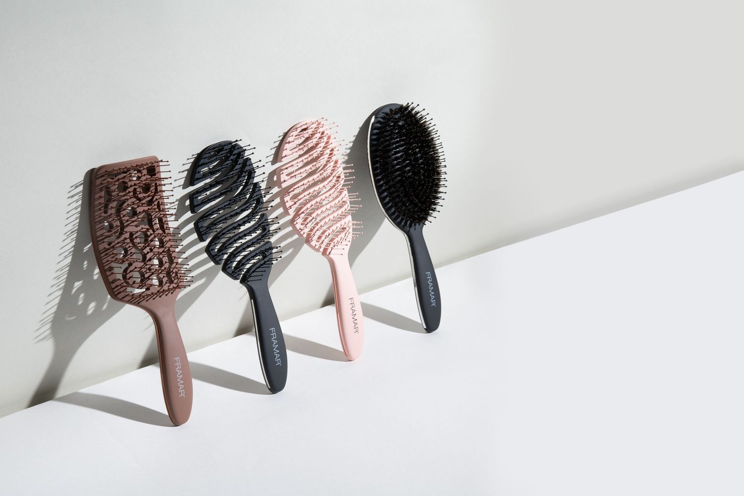 Studio product photography of detangling hair brushes in neutral and blush tones arranged on a clean, minimal backdrop.