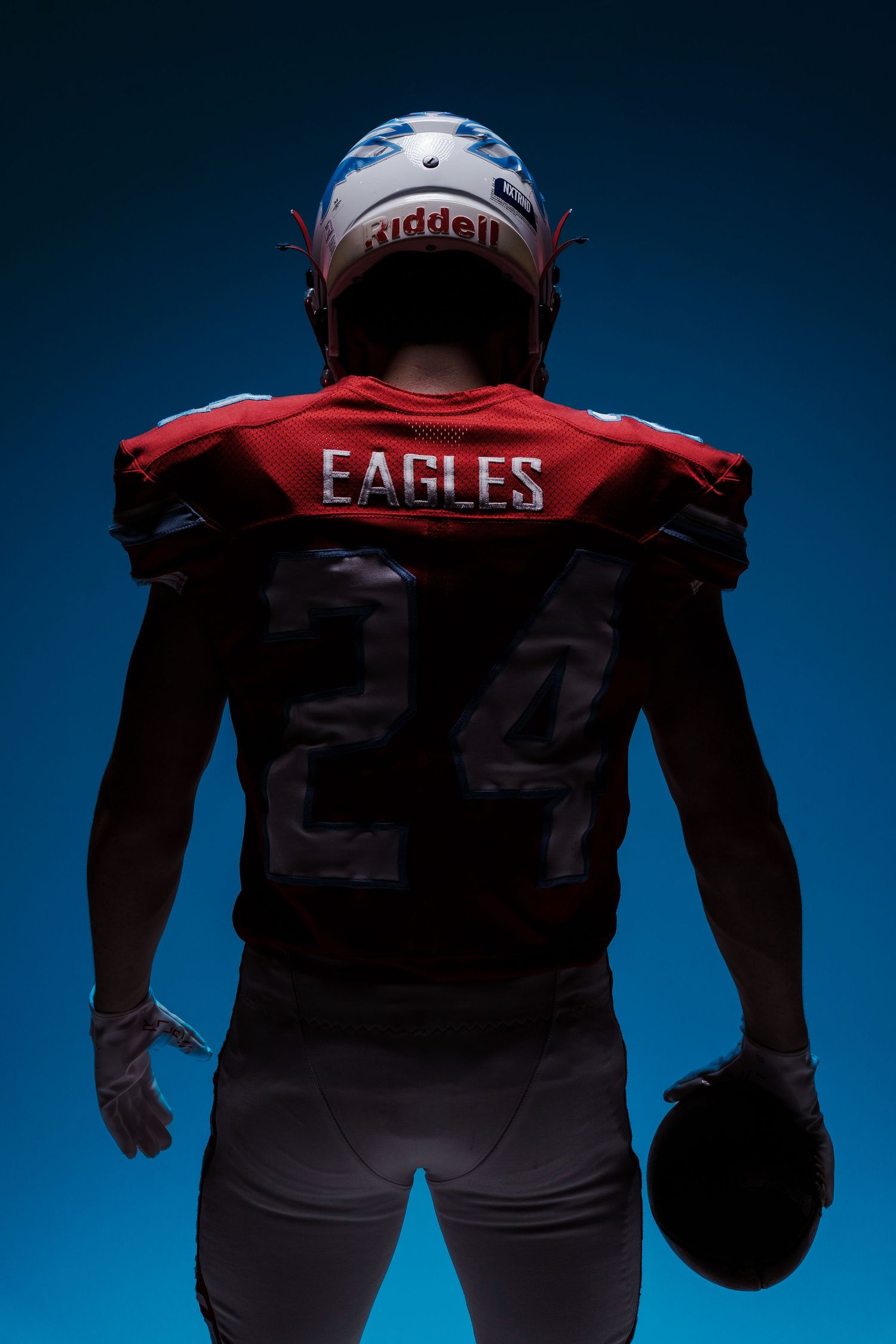 Football players in Eagles uniforms photographed from behind against blue backdrop.