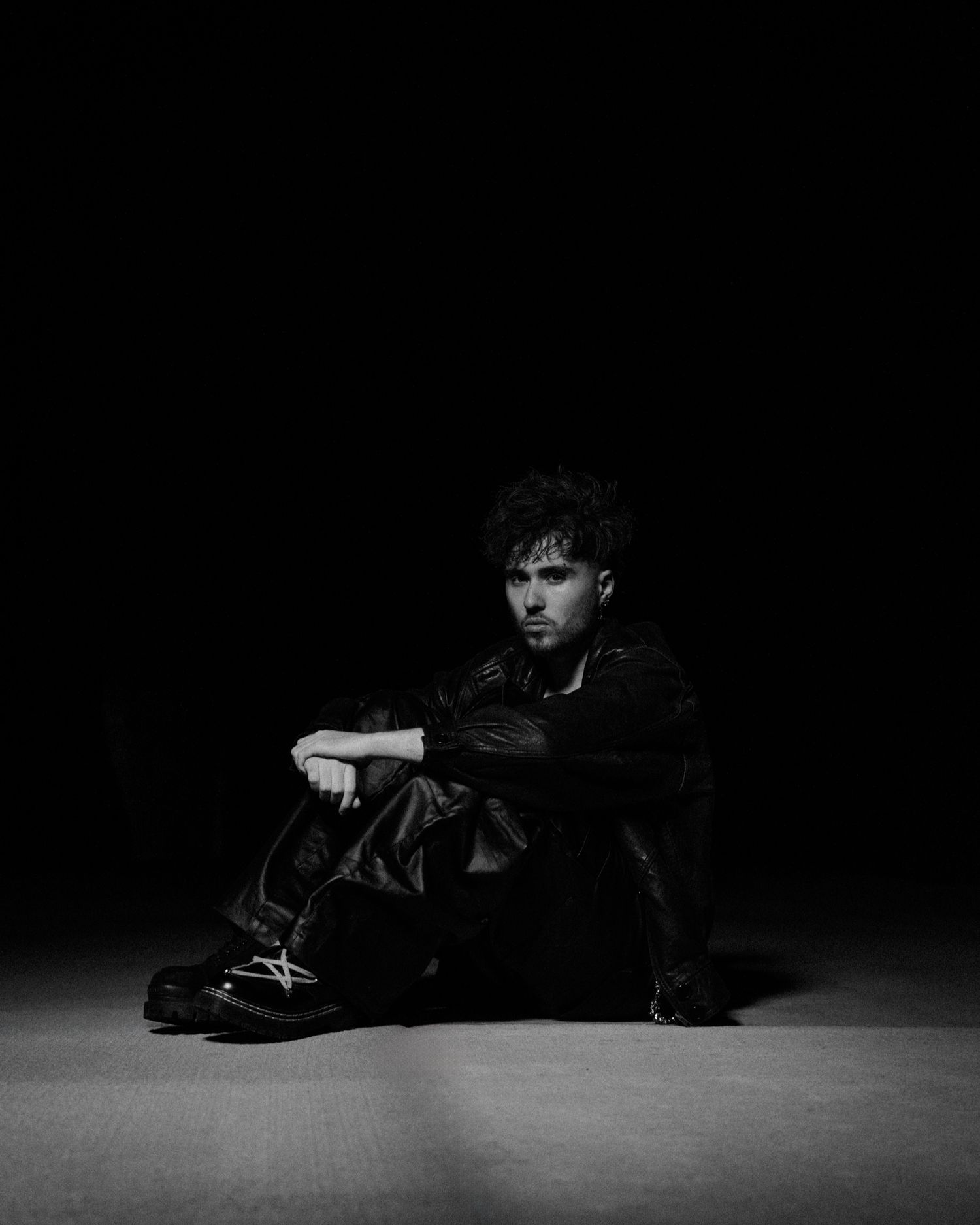 Dramatic black and white portrait in low-key lighting on dark floor.
