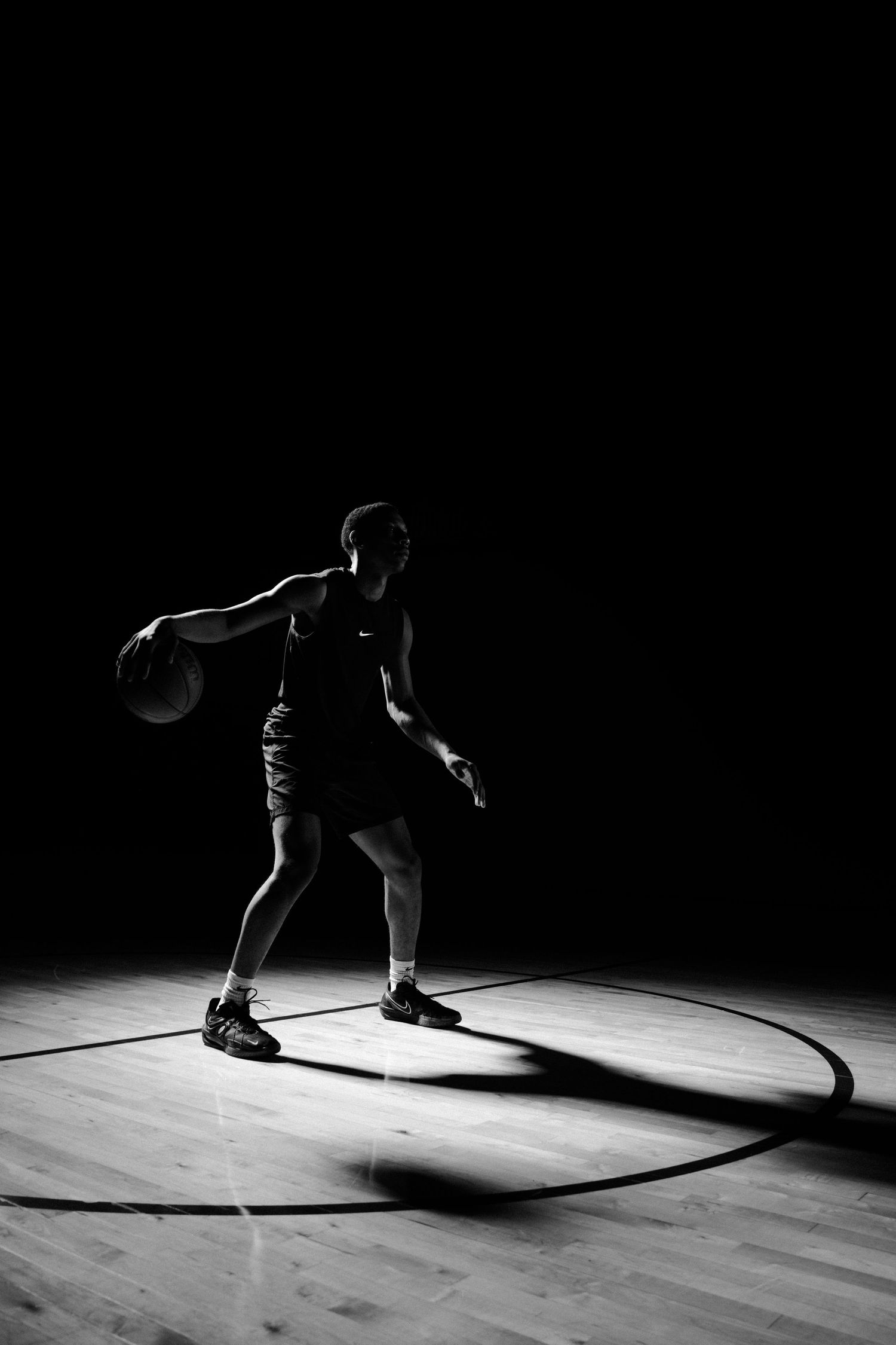 Silhouetted basketball player dribbling on wooden court in dramatic lighting.