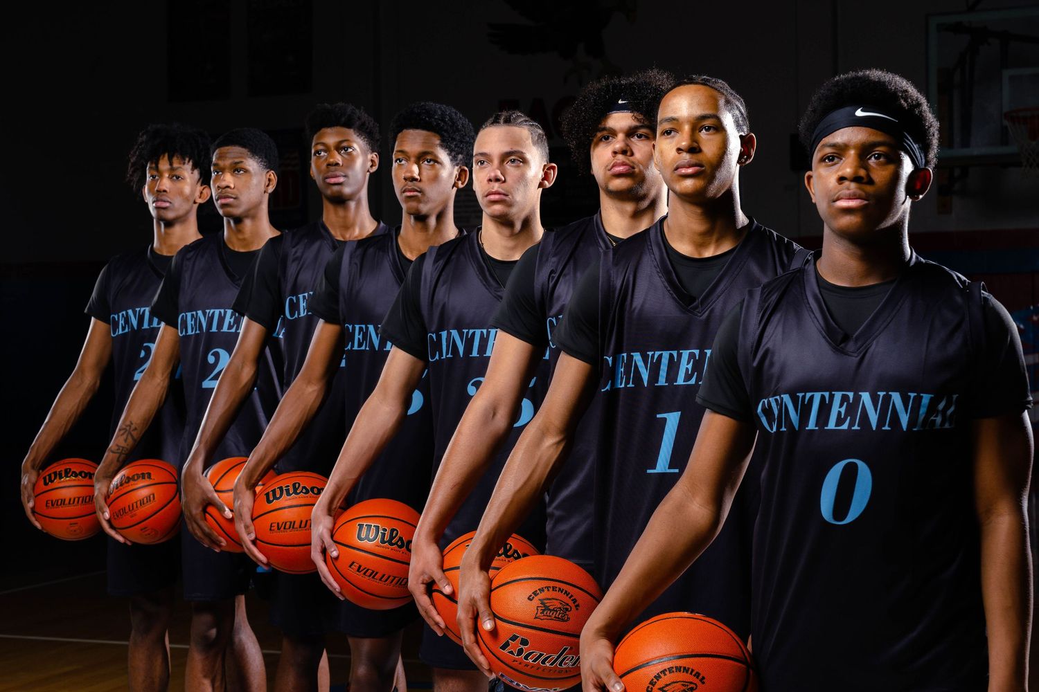 Basketball players pose in team uniforms while holding basketballs for a promotional photo shoot.