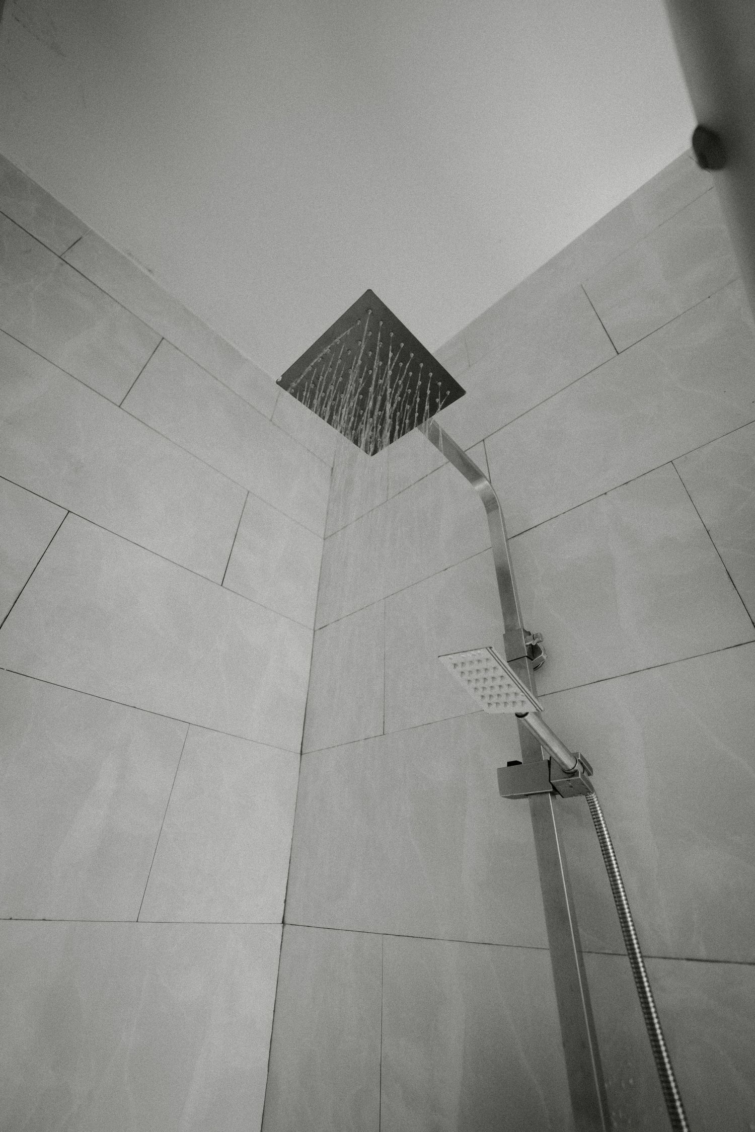 Modern shower head mounted on white tiled bathroom wall viewed from below.
