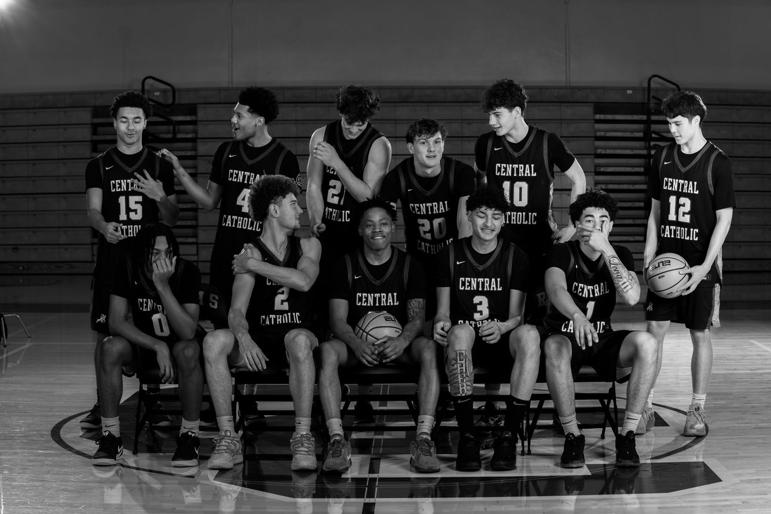 Basketball team members sit on court for dramatic black and white team photo.