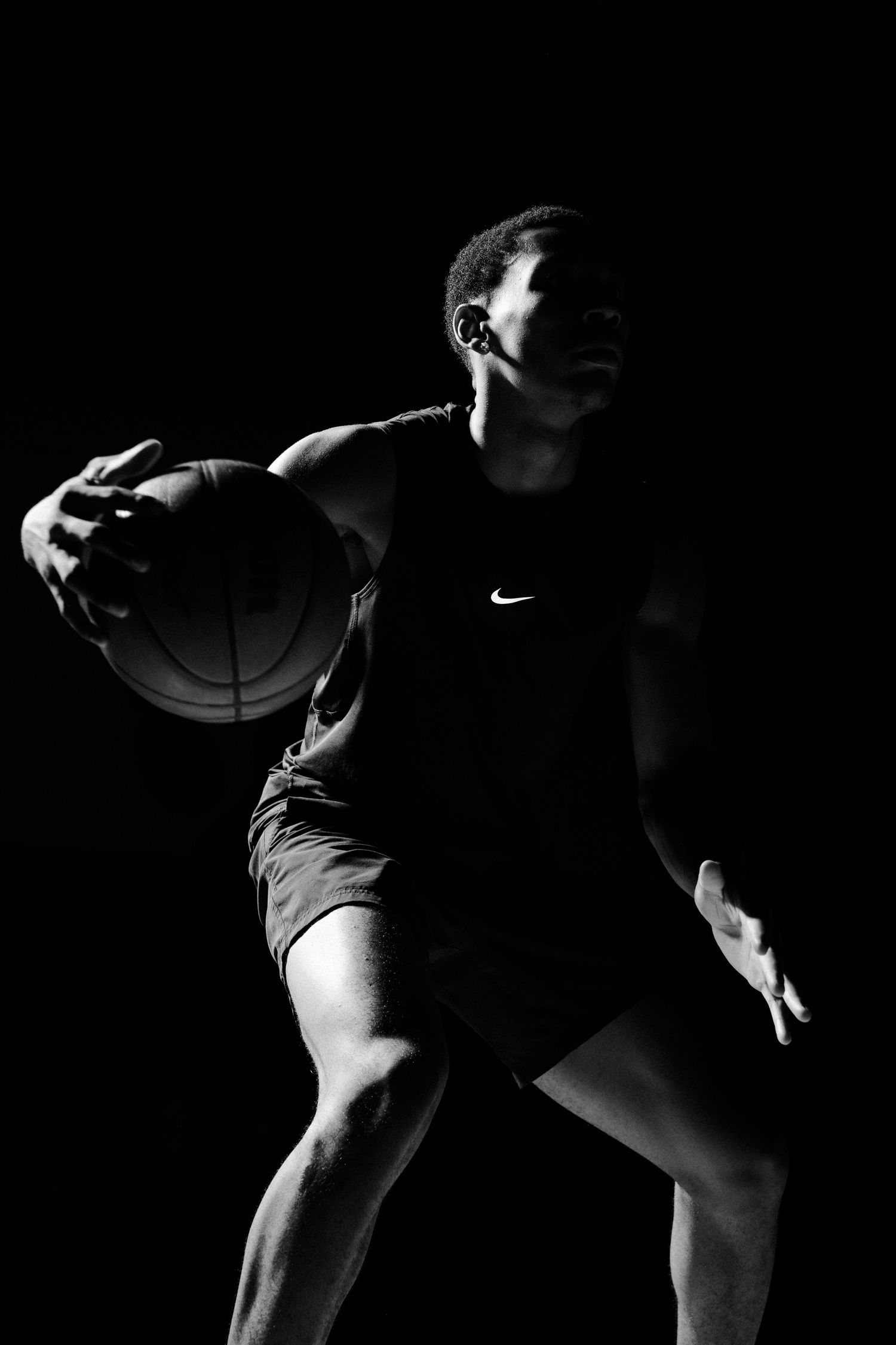 Dramatic side view of basketball player in Nike uniform holding ball against dark background.