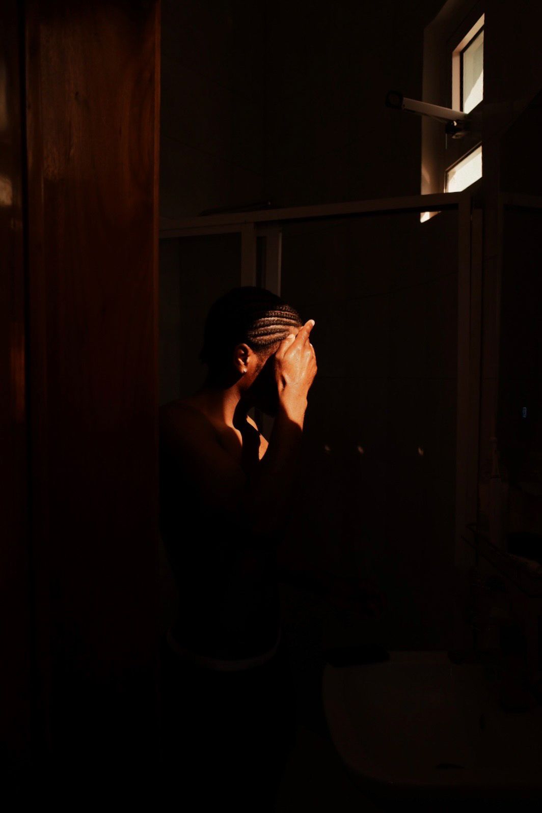 Moody indoor portrait with natural light streaming through window in darkness.