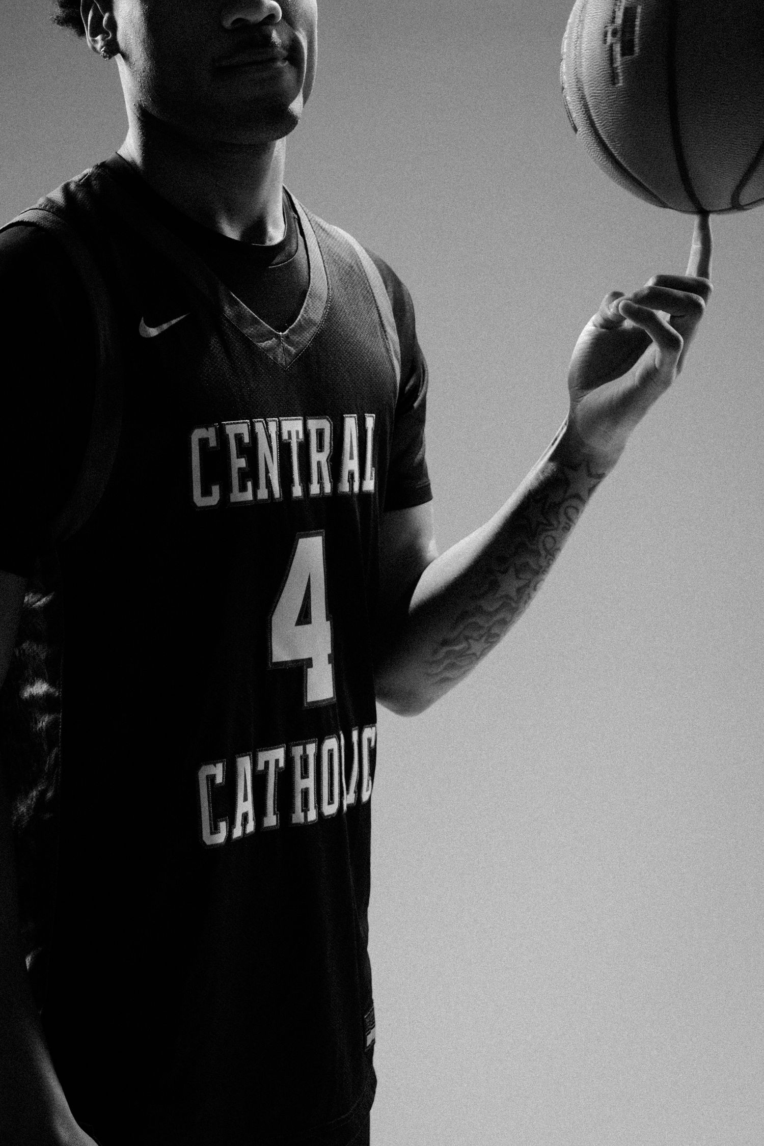 Basketball players in dark jerseys with Central Catholic branding stand in dramatic lighting.