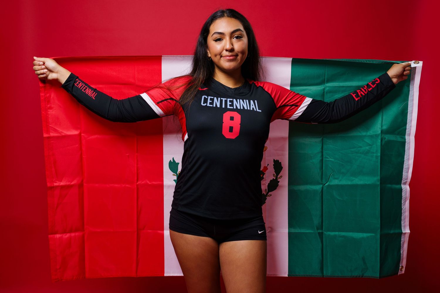 Athlete in black Centennial jersey number 8 poses with red and green flag against colorful wall background.
