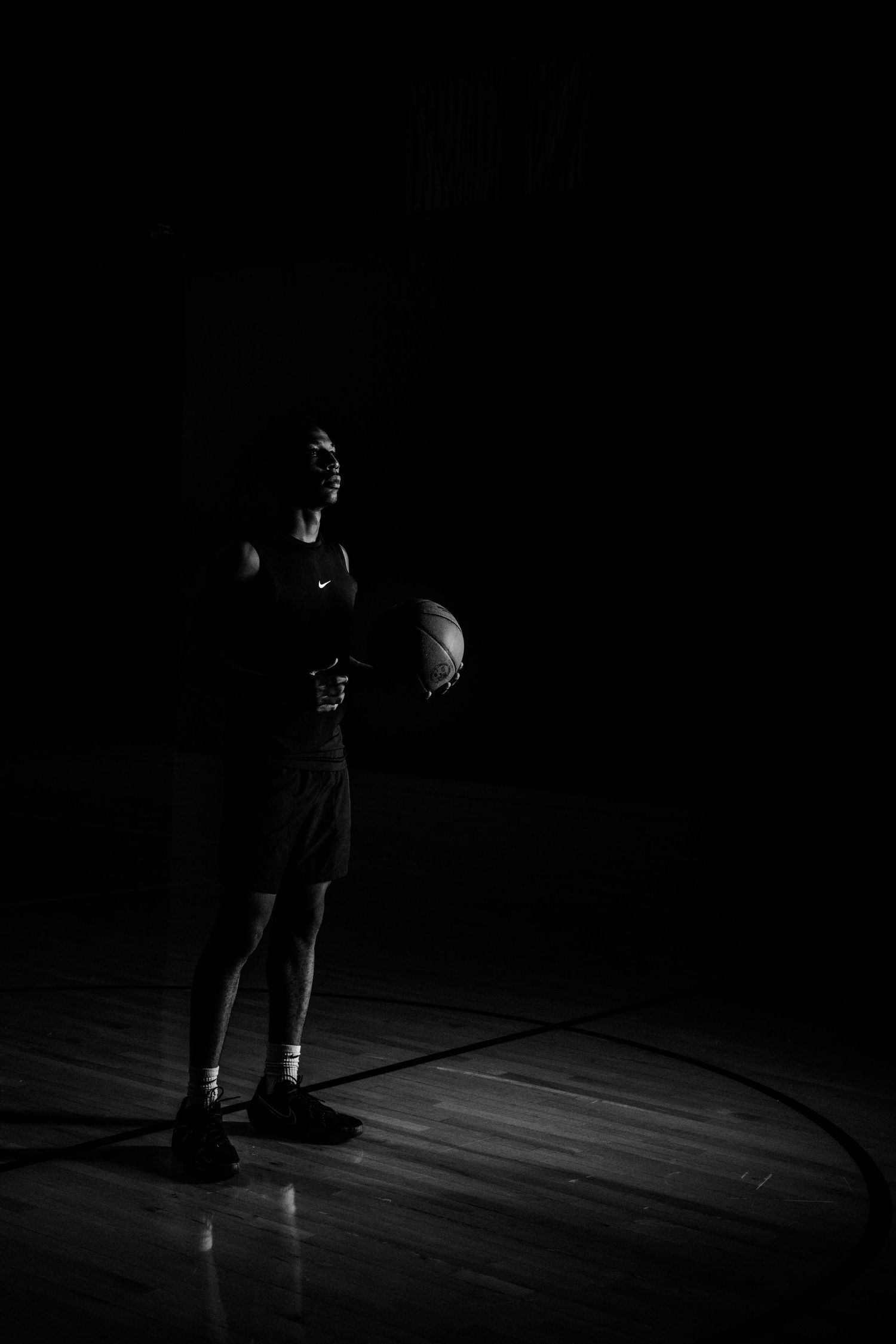 Basketball player stands in dramatic lighting on a wooden court.