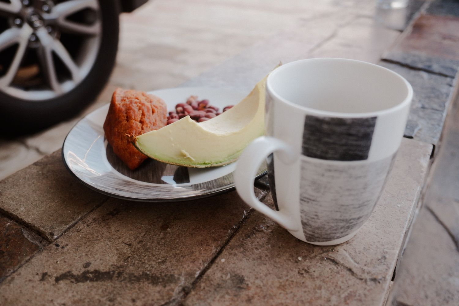 Coffee cup and plate on wooden surface with partial car wheel visible.