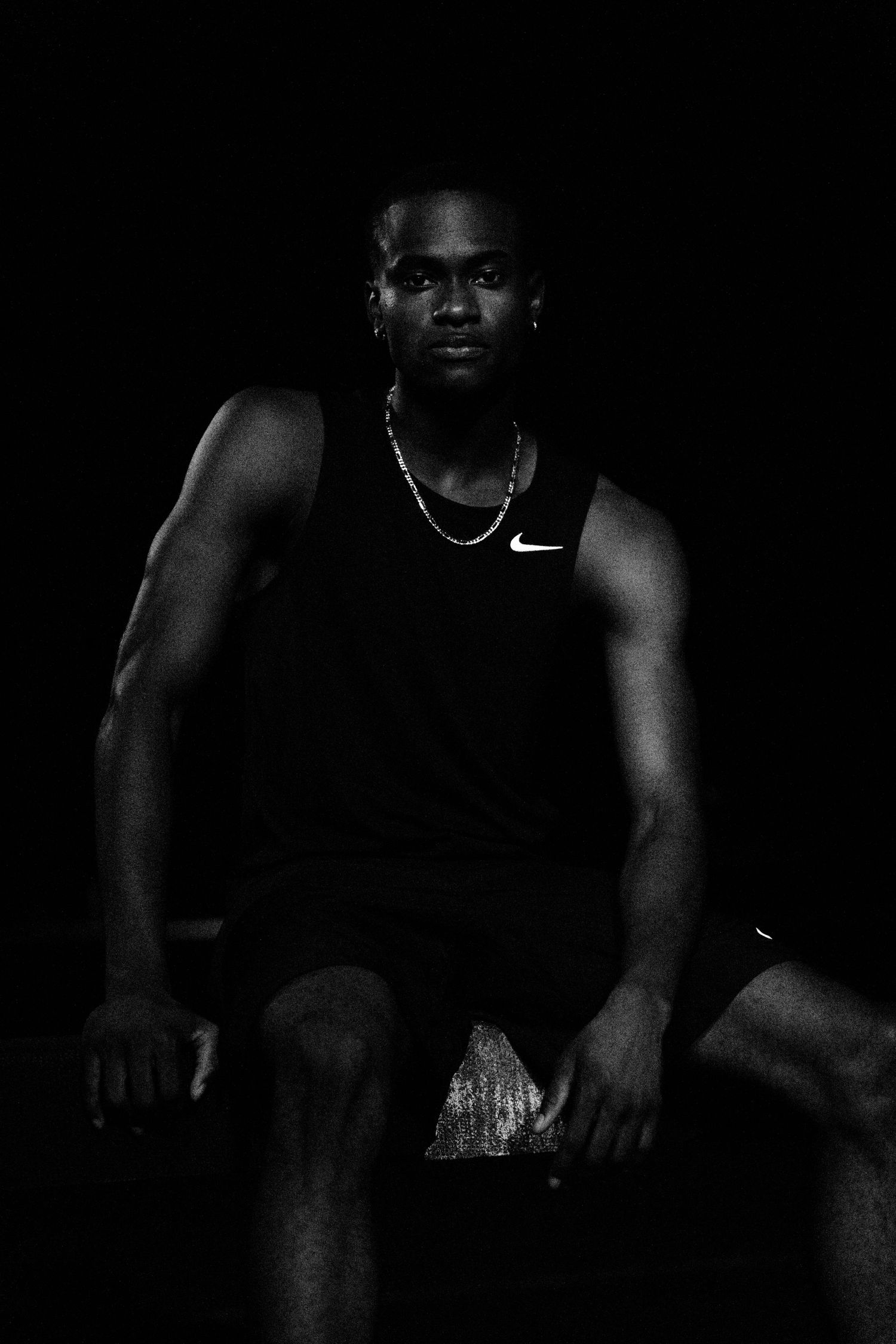 Athletic Black man in Nike tank top seated confidently, dramatic black and white studio portrait.