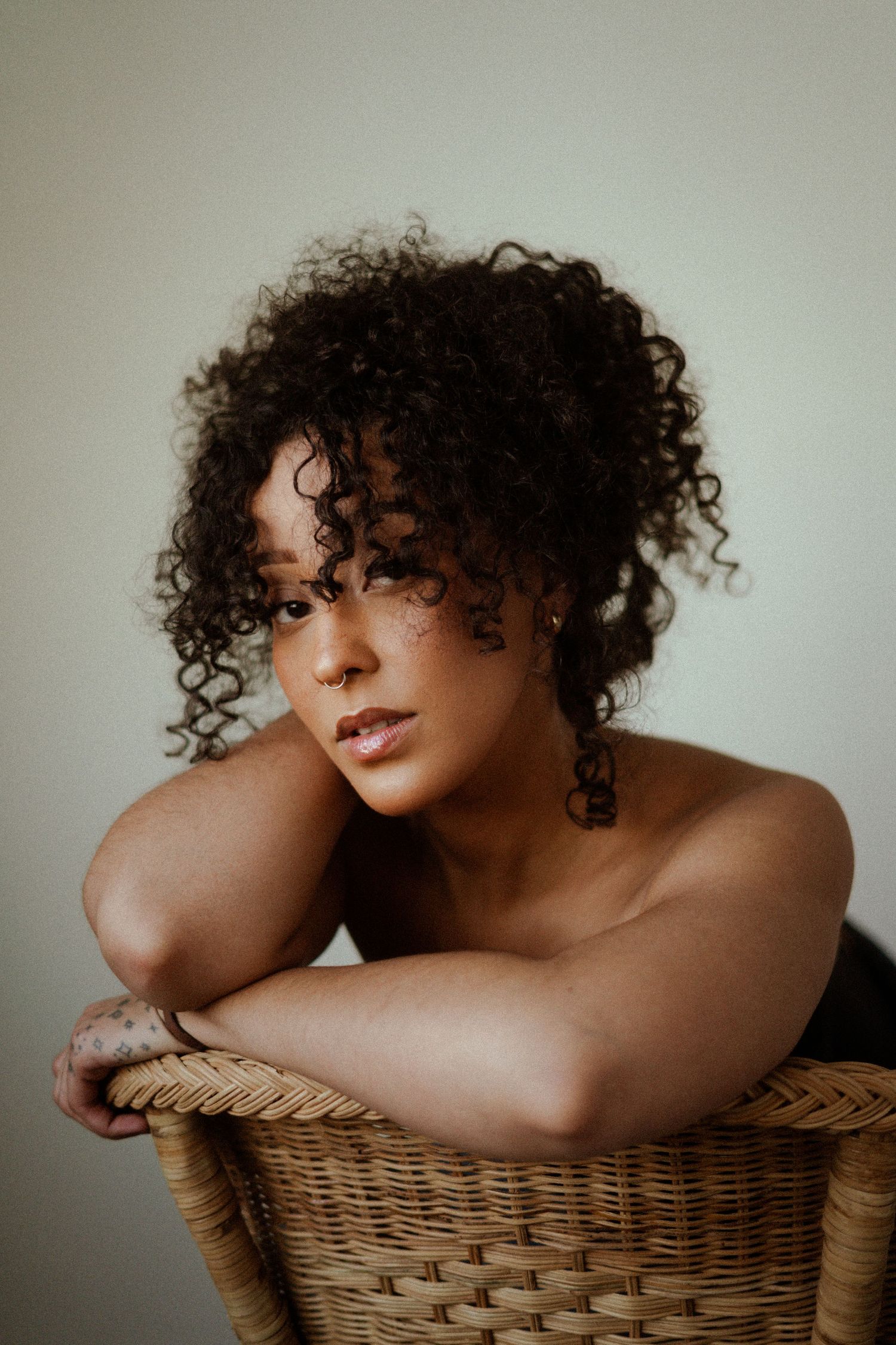 Intimate portrait series showing artistic poses with curly hair and wicker furniture.