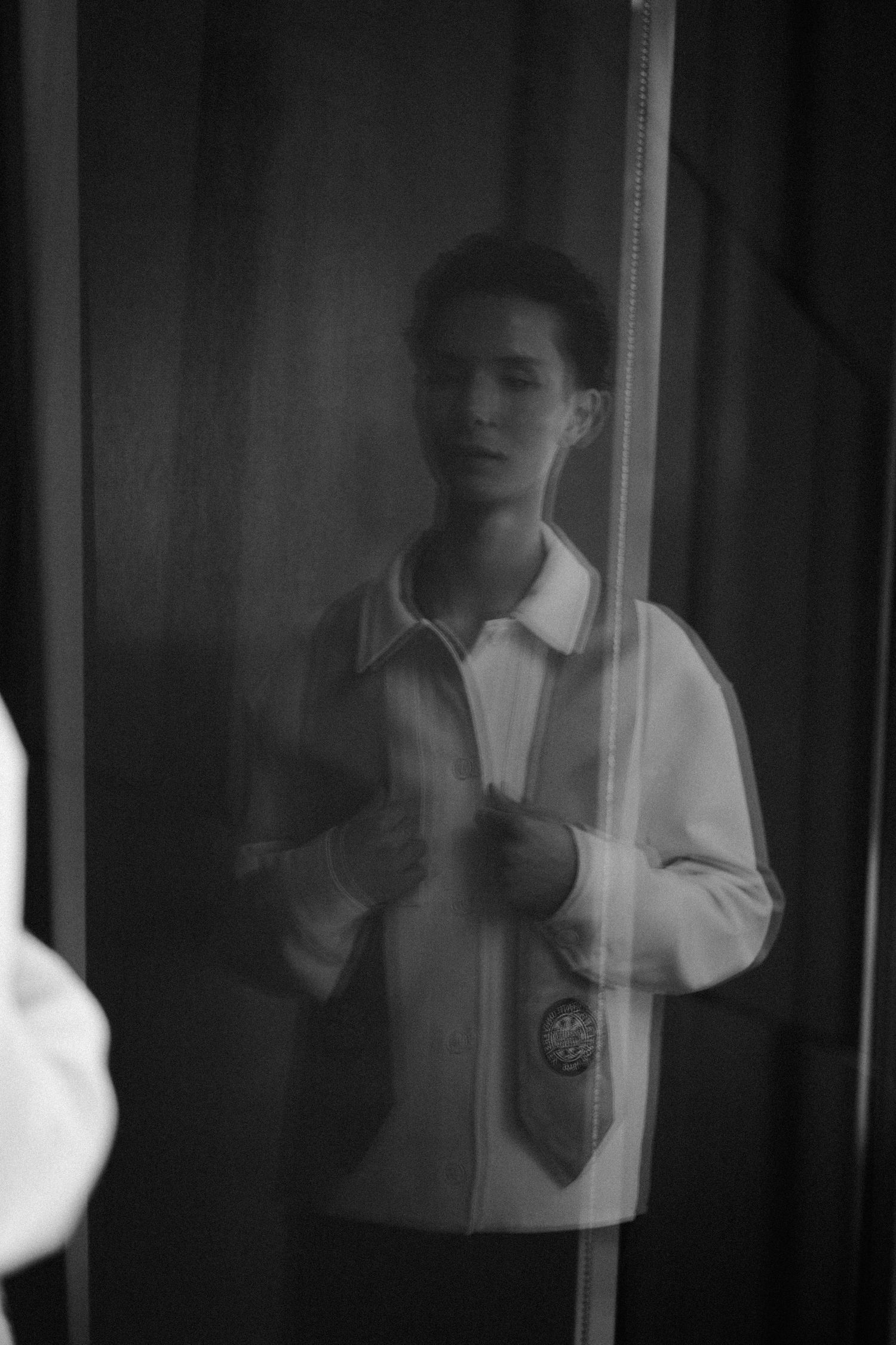 Black and white photo of a young man adjusting his tie, reflected in a mirror.