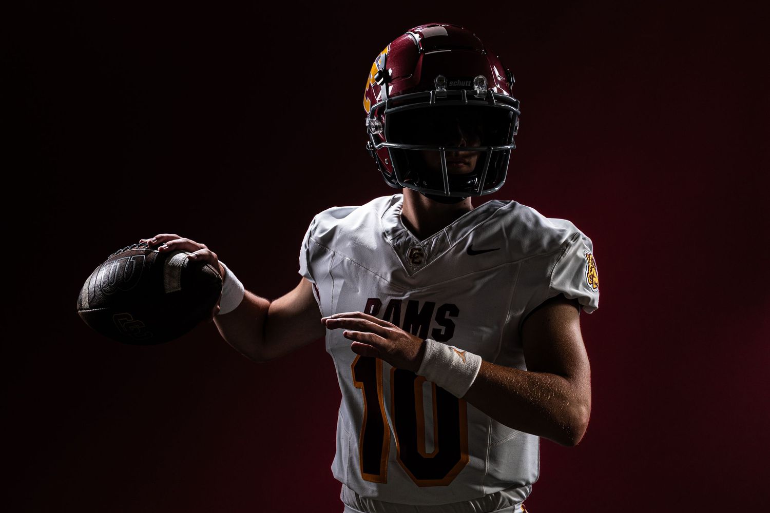 Football player wearing number 10 Rams jersey poses in dramatic dark lighting holding a football in throwing position.