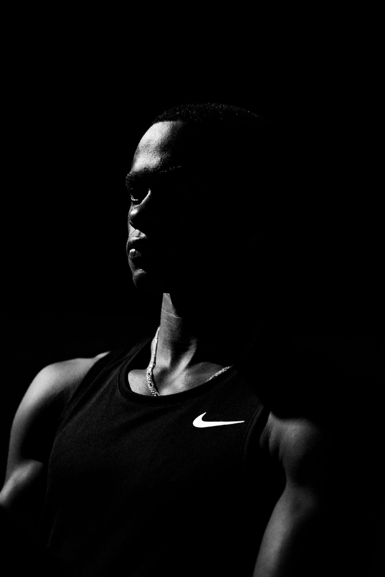 Black and white portrait of an athlete wearing a Nike tank top, dramatically lit against a dark background.