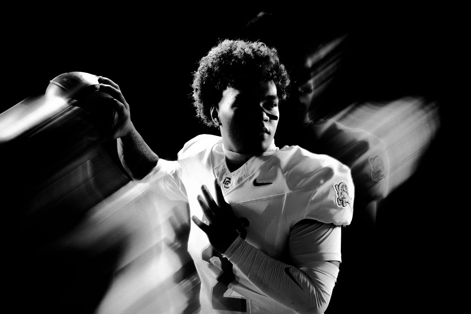 Black and white photo of a football player in uniform holding a ball, captured with dynamic motion blur effect.