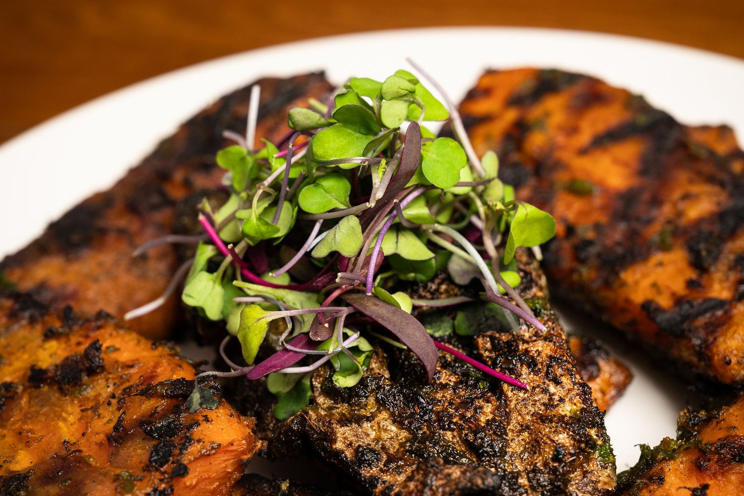 Grilled blackened chicken breasts topped with fresh microgreens and red cabbage sprouts on a white plate.