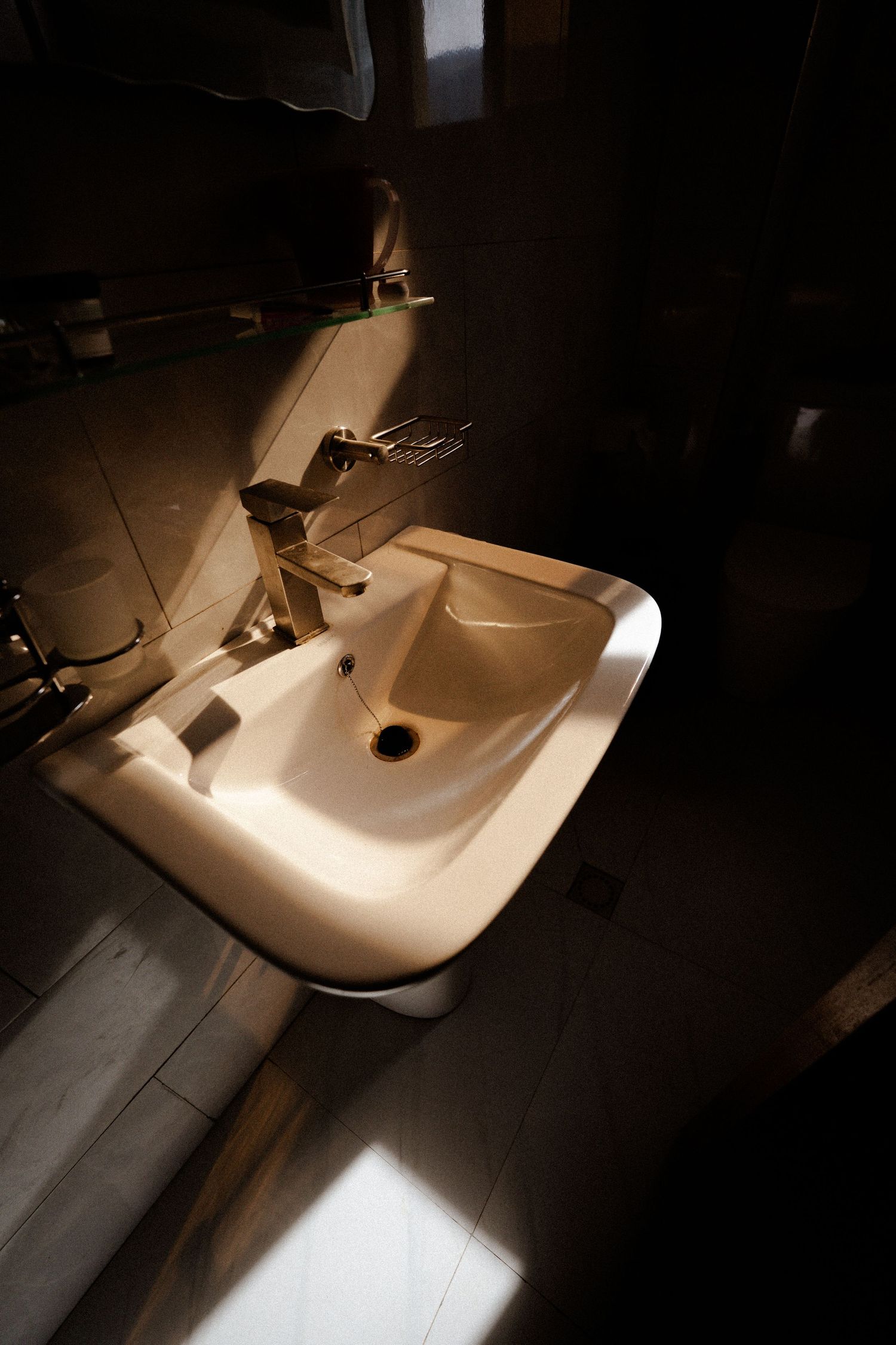 A white bathroom sink illuminated by dramatic lighting in a dark room.