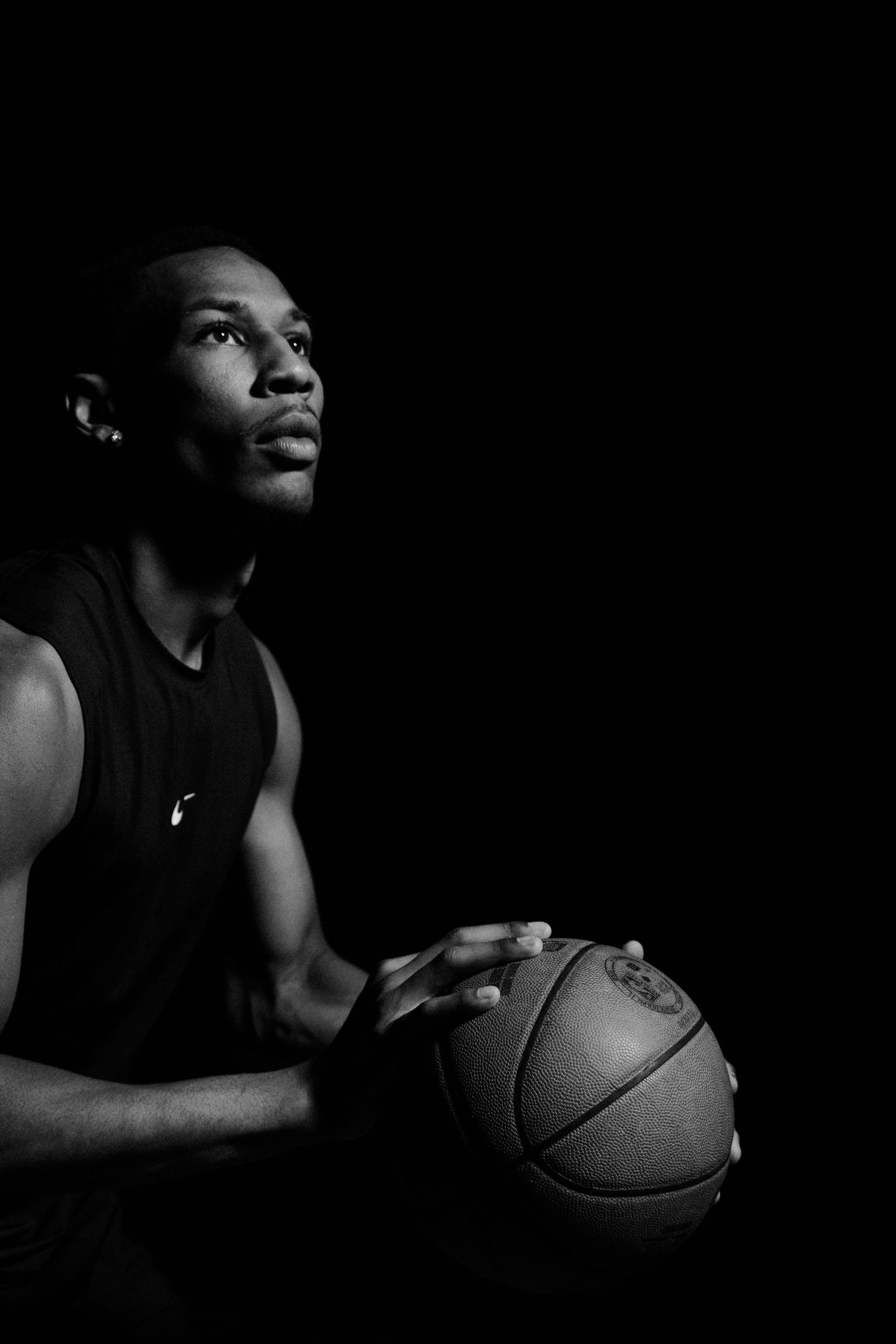 Basketball player holding ball in moody low-key lighting.