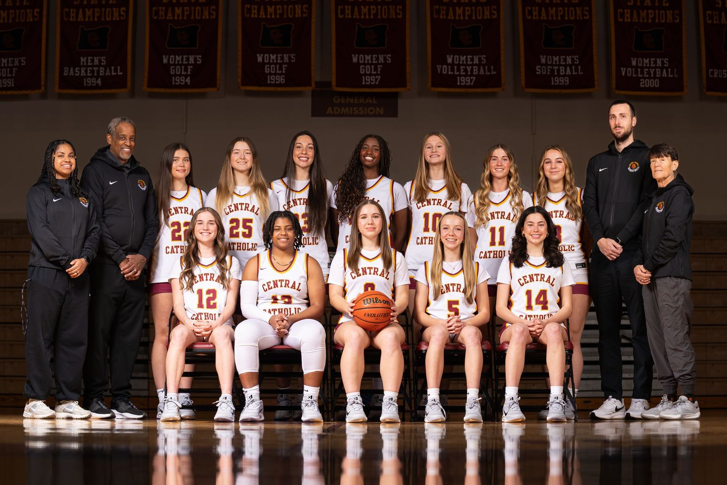 Basketball team group photo with players and coaches lined up on gym floor.