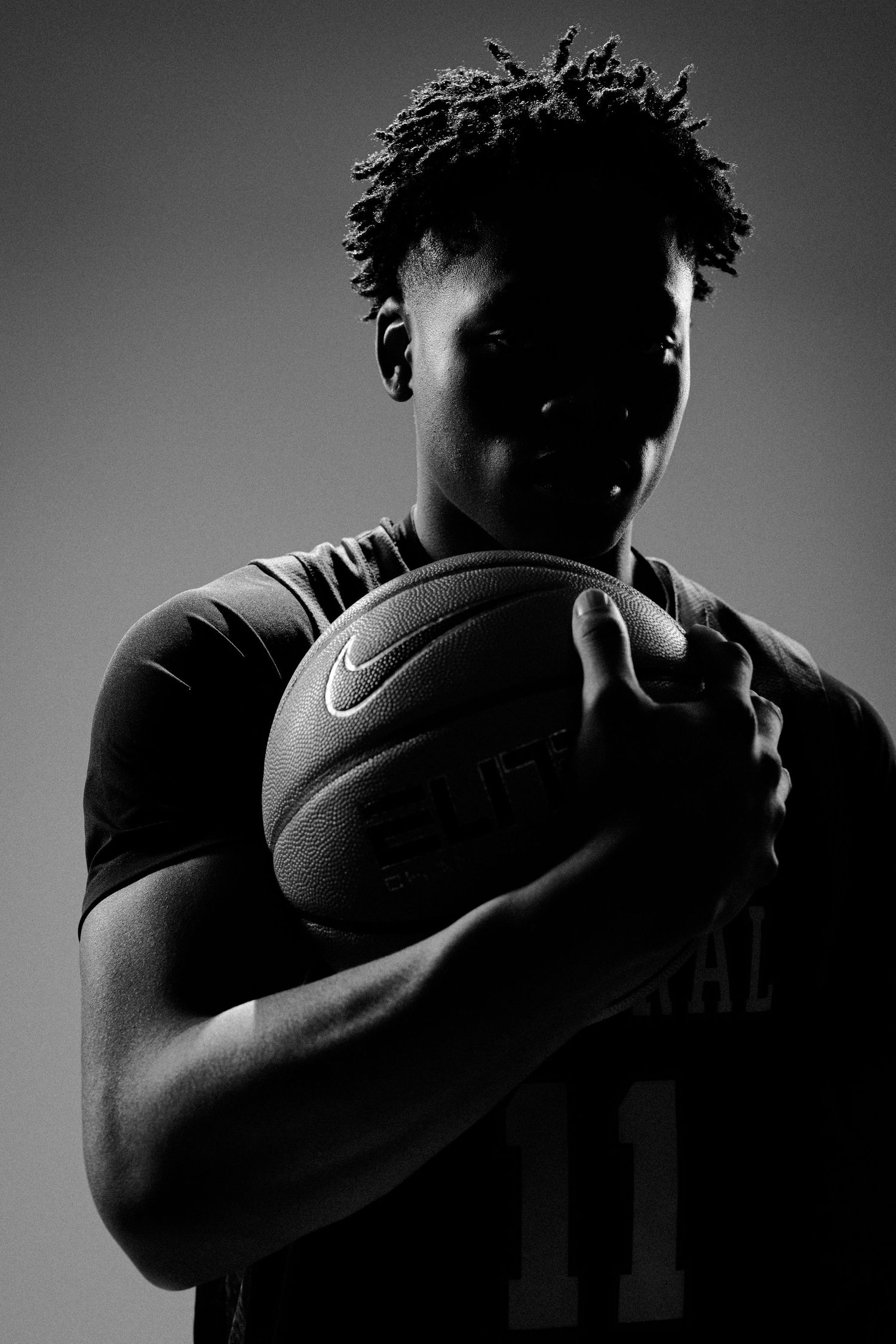 Basketball player in dark jersey holds ball in dramatic side-lit portrait series.