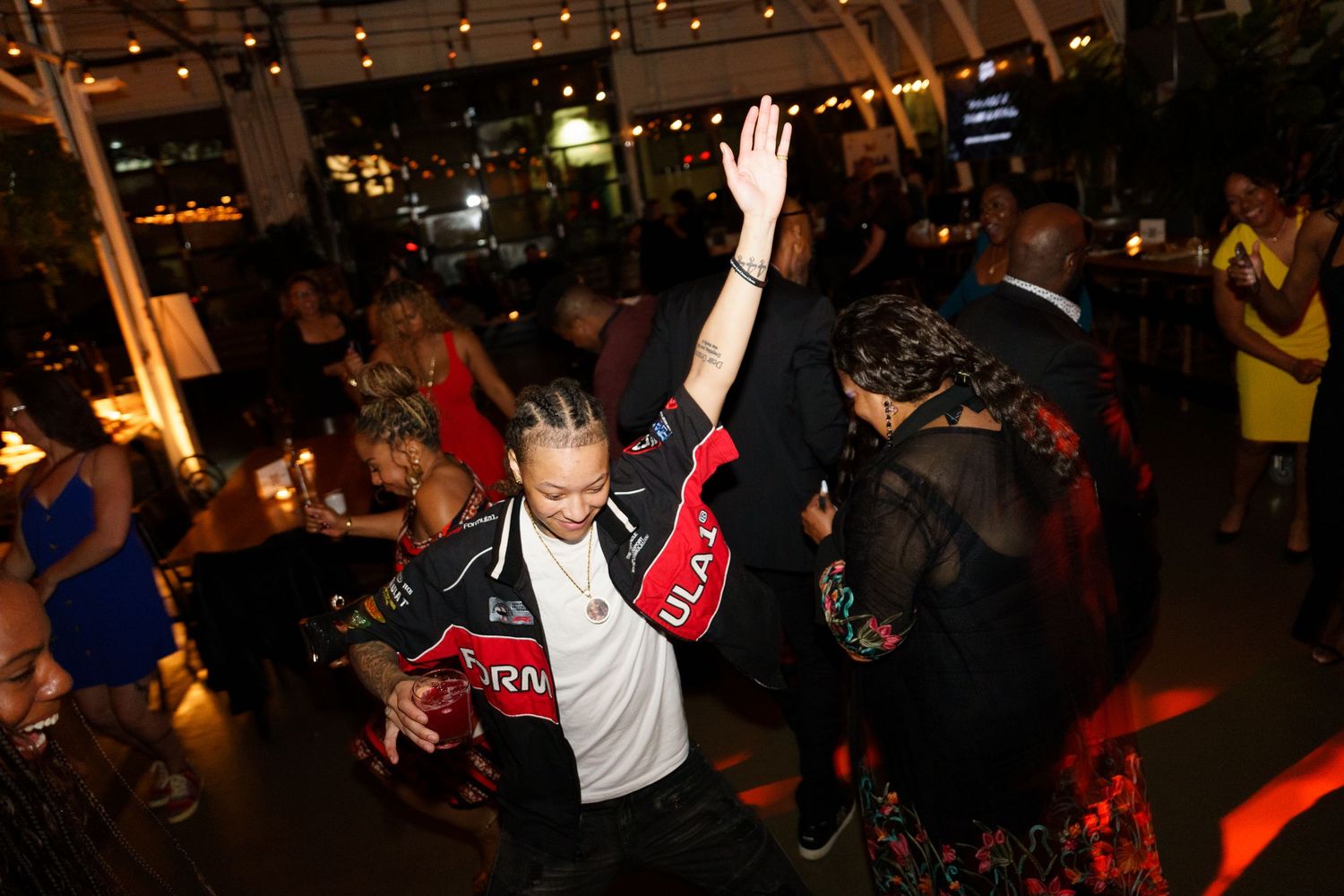 People dancing energetically at a lively indoor party event with string lights and a crowded dance floor.