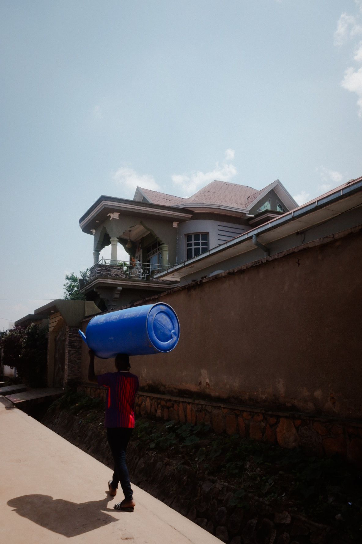 Person carrying a large blue rolled item past residential buildings.