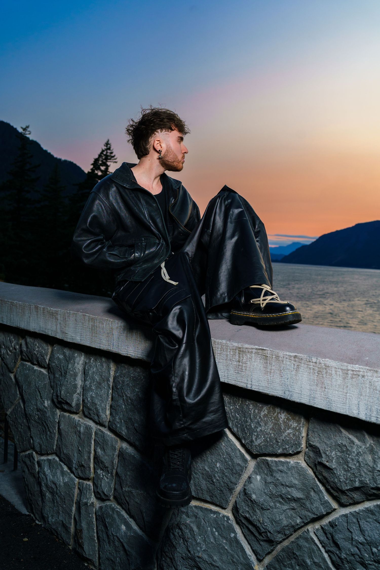 Person in black jacket looking out over scenic mountain landscape at sunset.