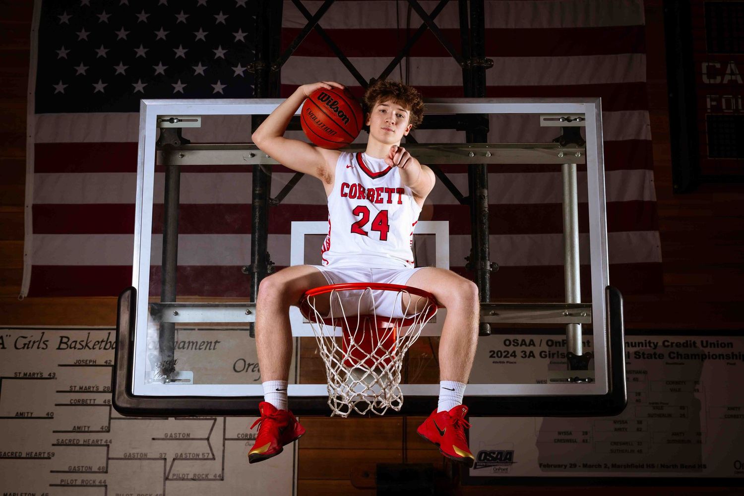 Basketball player poses in front of American flag backdrop in red and white uniform for sports portrait.