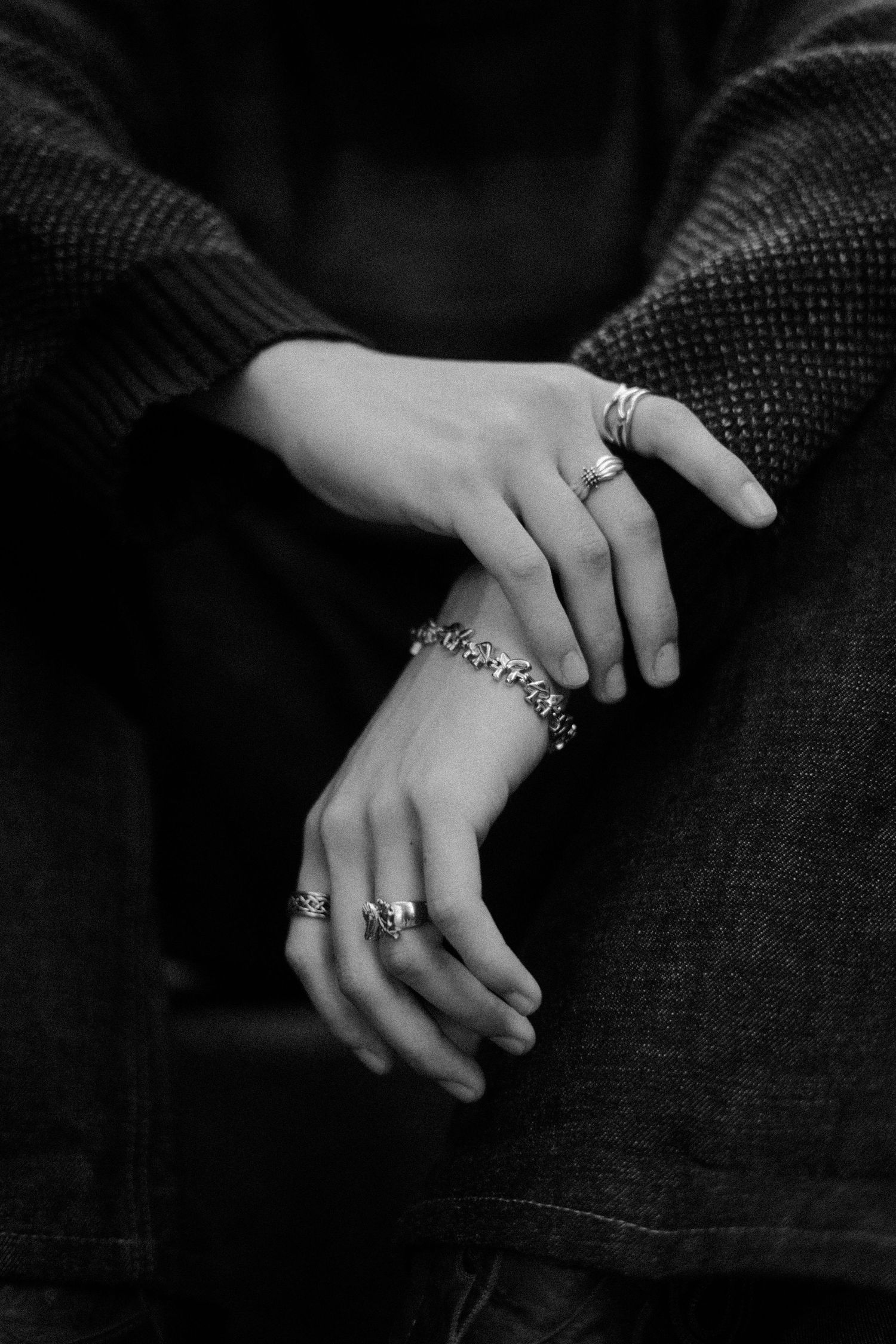 Close-up of hands with rings resting on dark denim fabric.