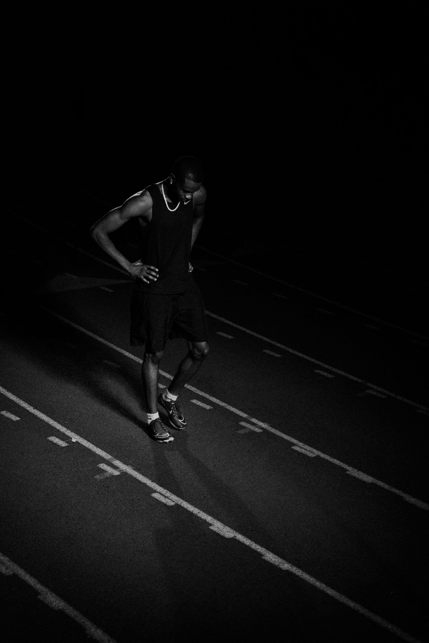 Black and white photo of a male athlete with a prosthetic leg standing on a running track at night.