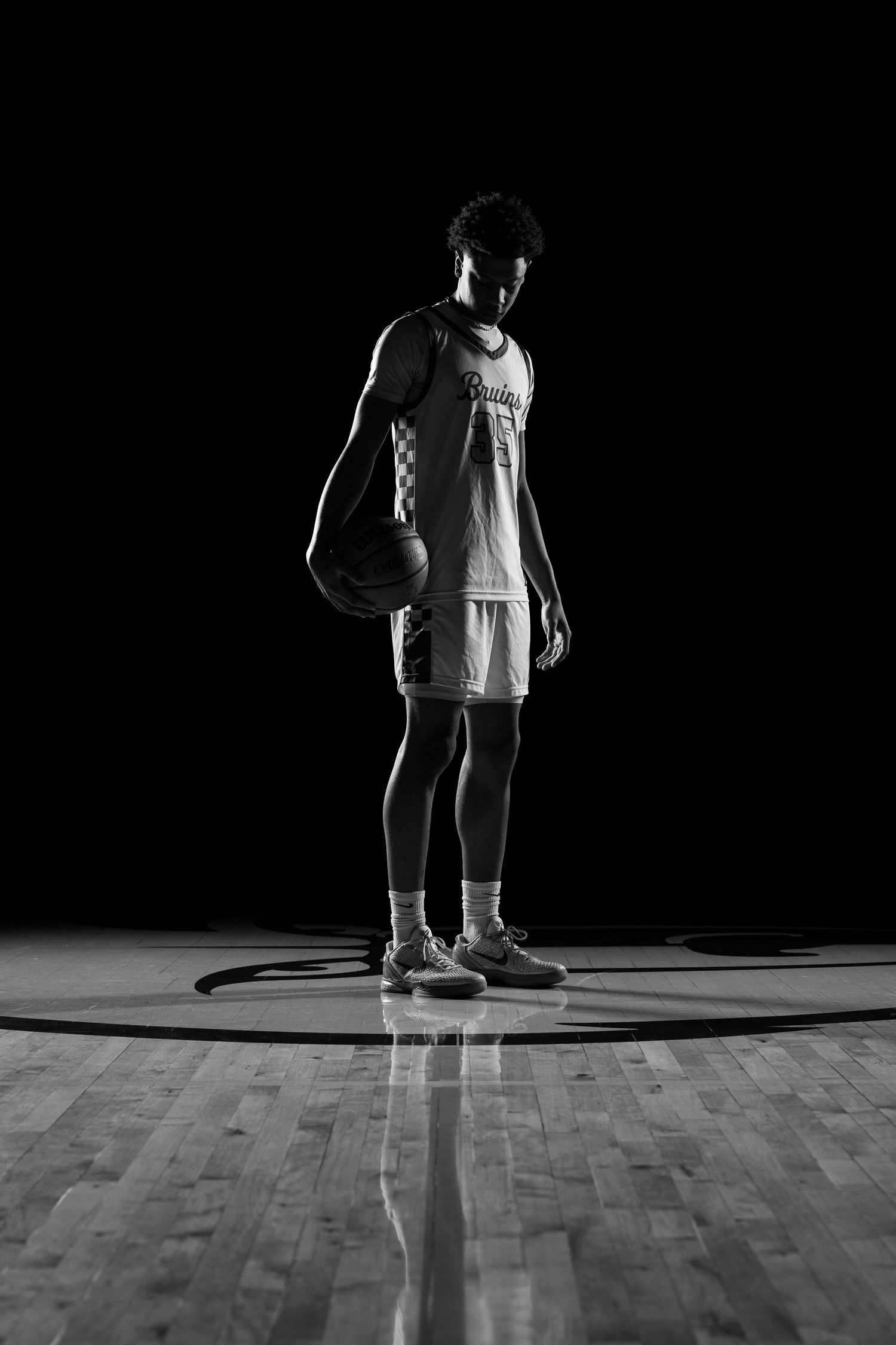 Dramatic silhouette of basketball players on wooden court with harsh lighting.