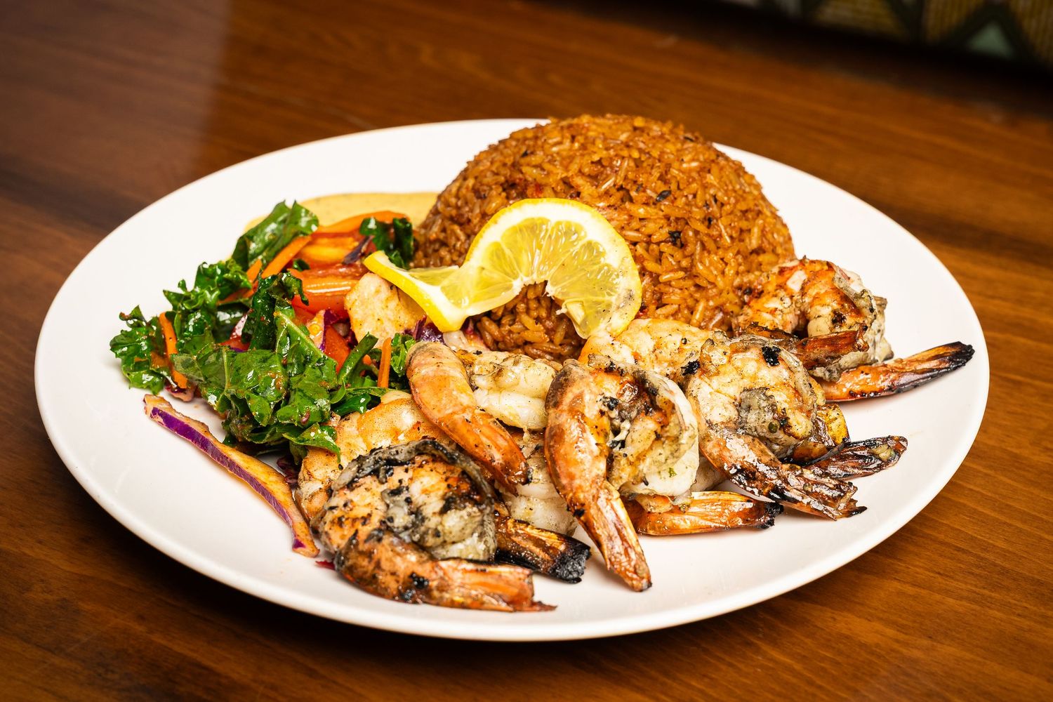 Grilled shrimp platter with lemon, seasoned rice, and fresh salad on a white plate.