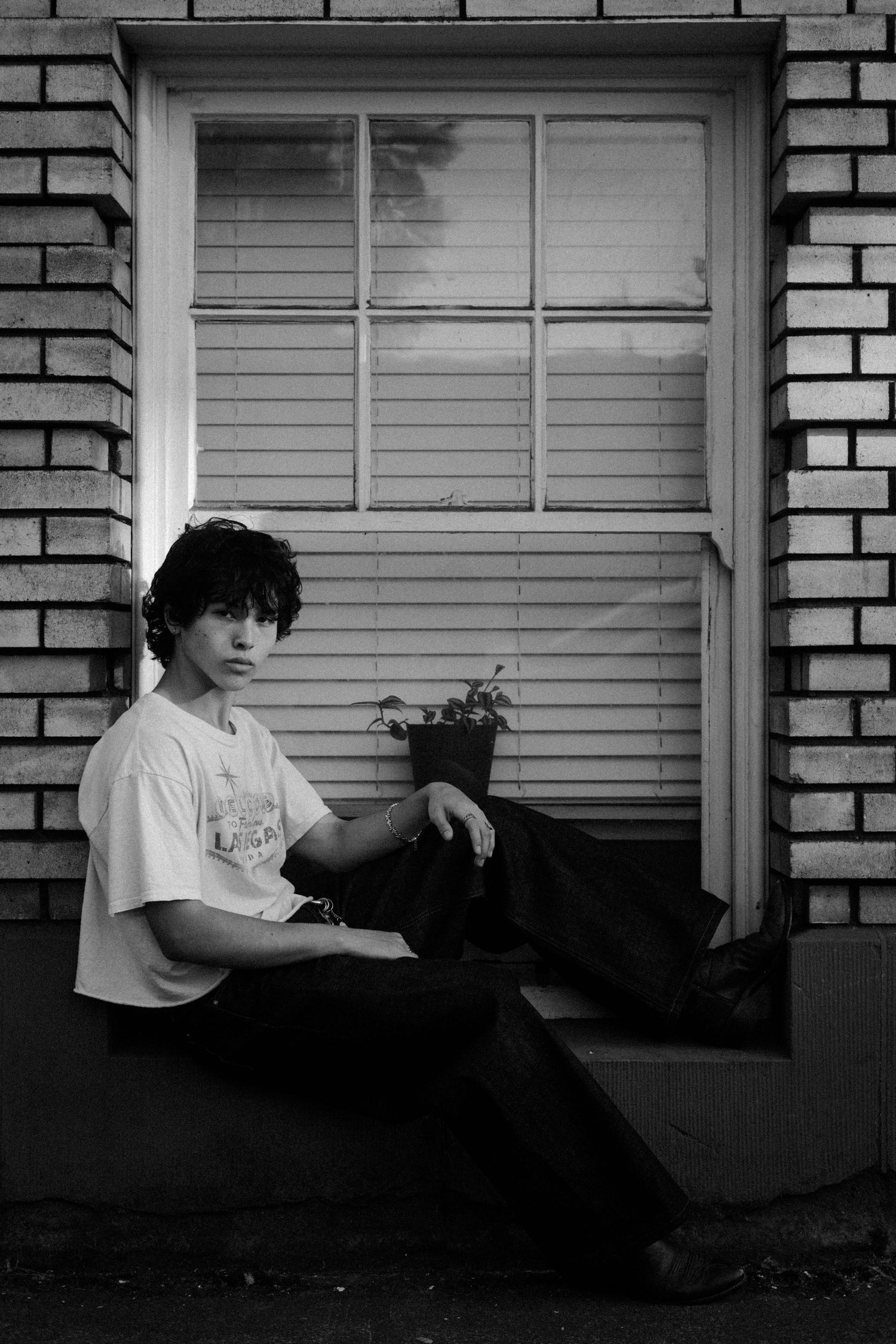 Black and white series showing figure resting against brick building with window.