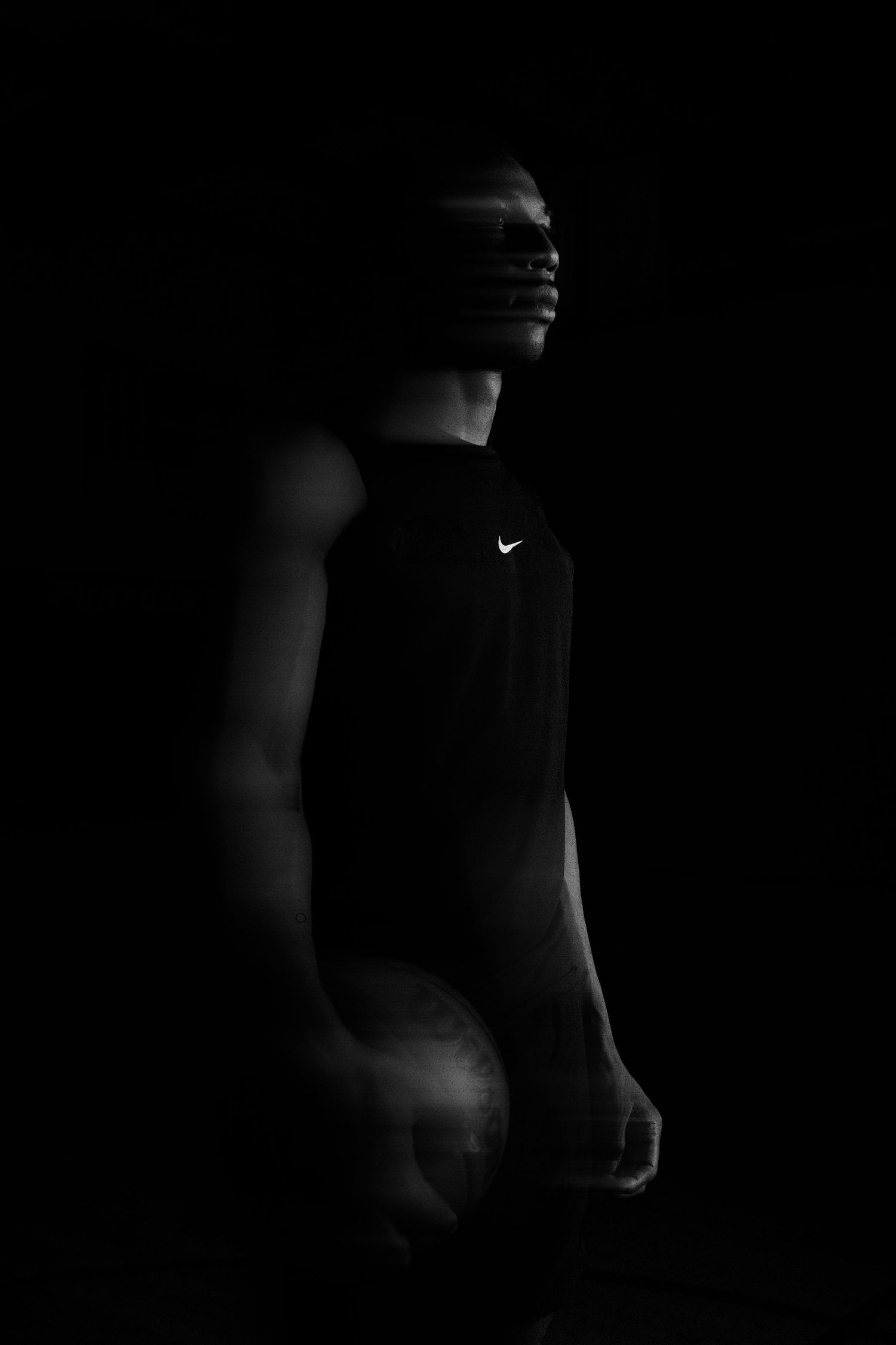 Dramatic black and white portrait of an athlete in Nike apparel emerging from darkness.