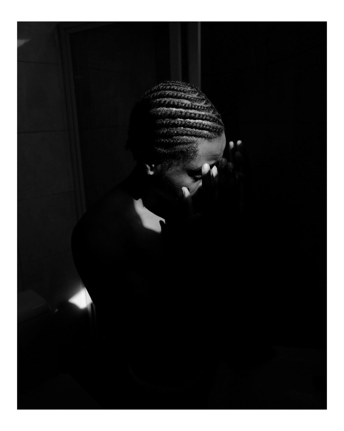 Dramatic low-key portrait in darkness with light falling on a person wearing braids.