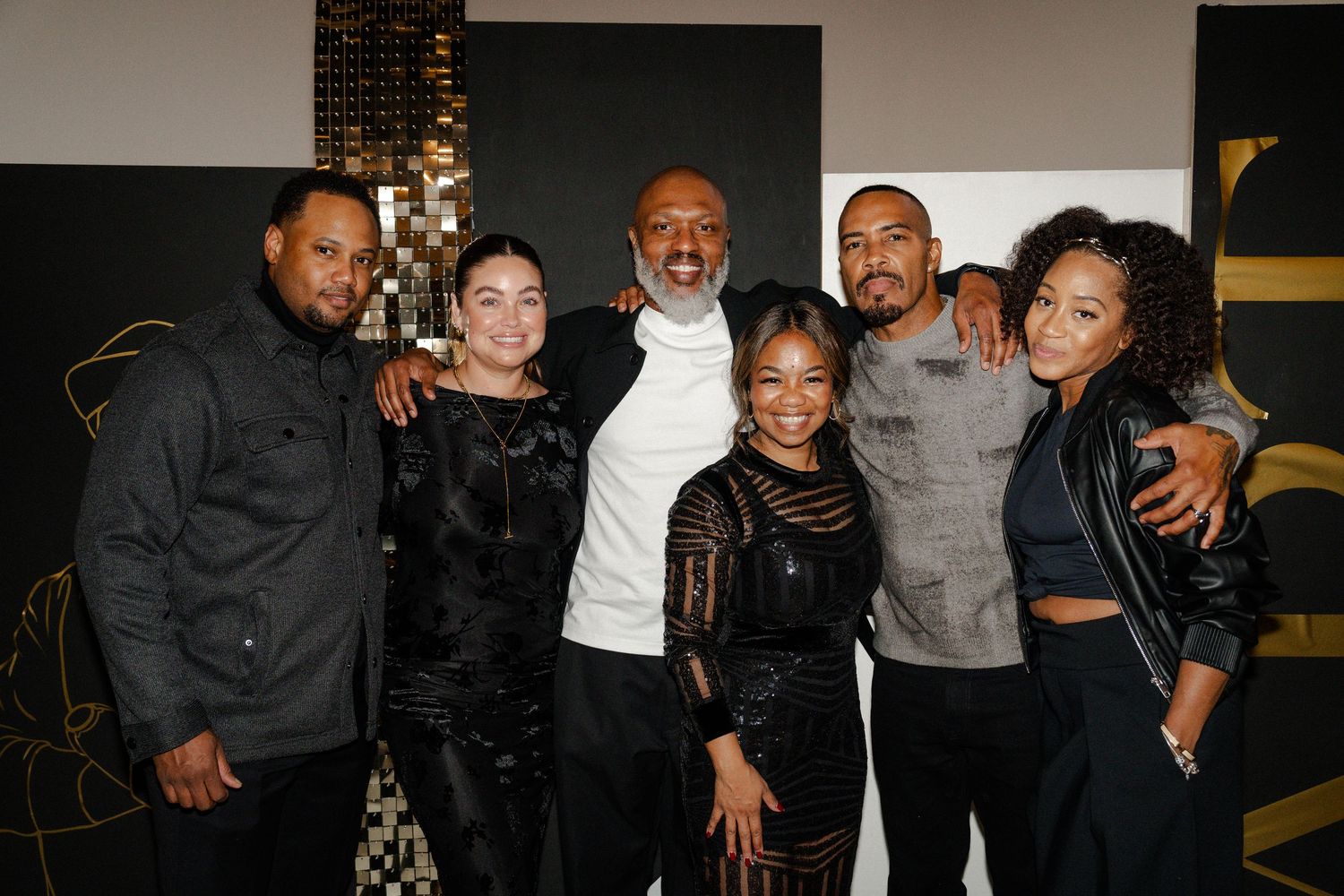 Group of six people smiling and posing together at a stylish black and gold event venue.