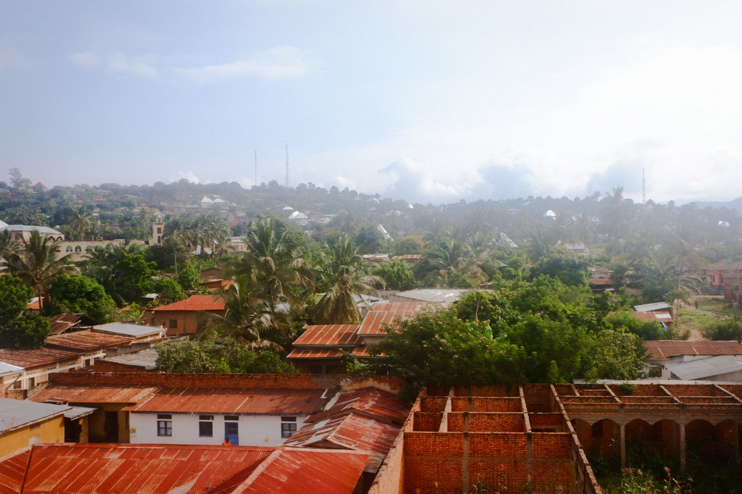 Panoramic view of red-tiled roofs and palm trees in a coastal city landscape.