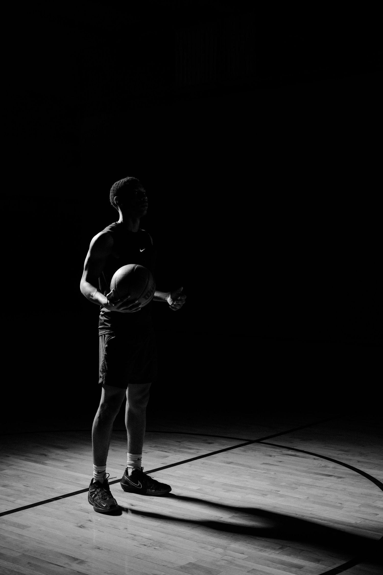 Athletic figure in dramatic side lighting performs on a basketball court.