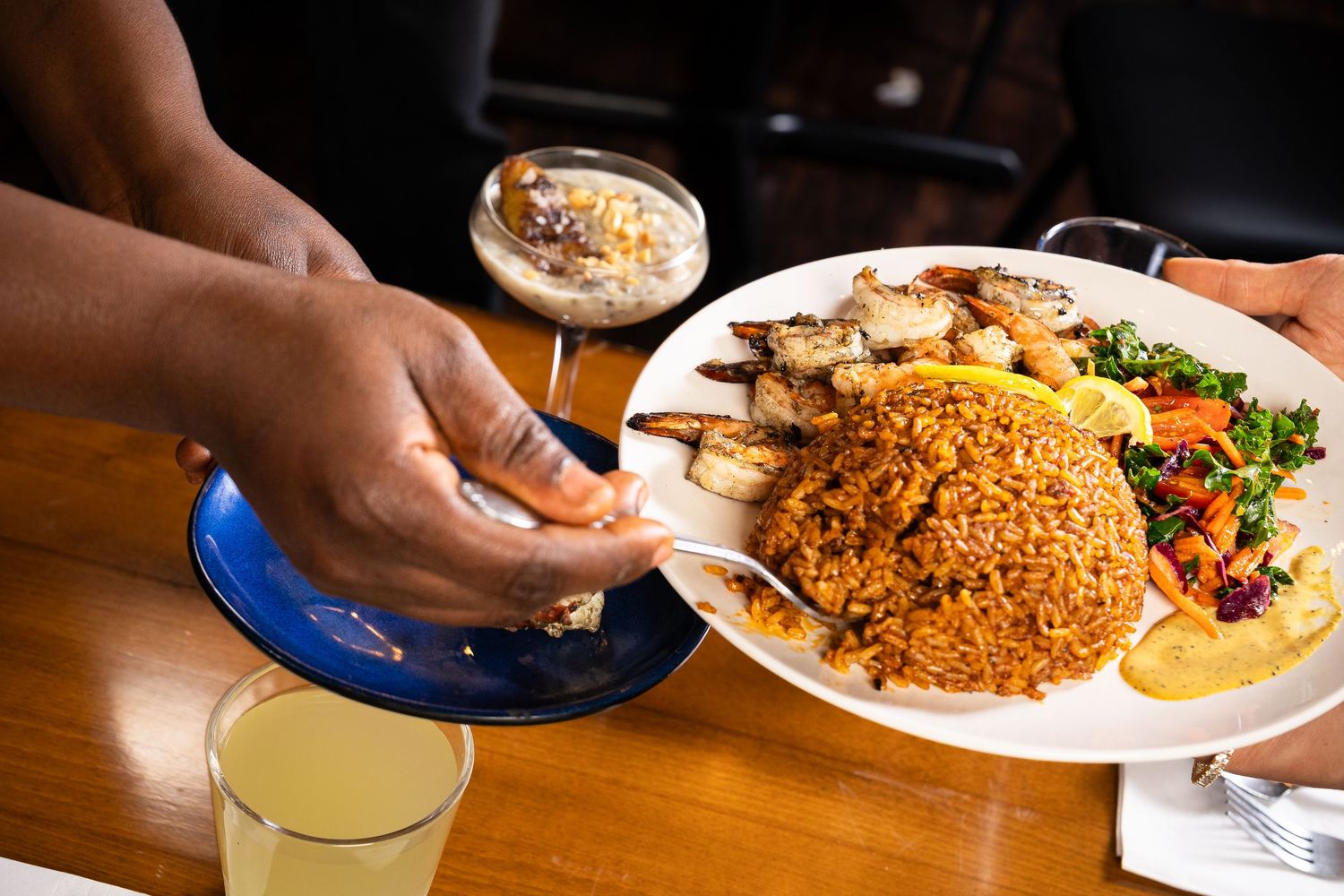 A plate of jollof rice with grilled fish, vegetables, and lemon served at a restaurant table.