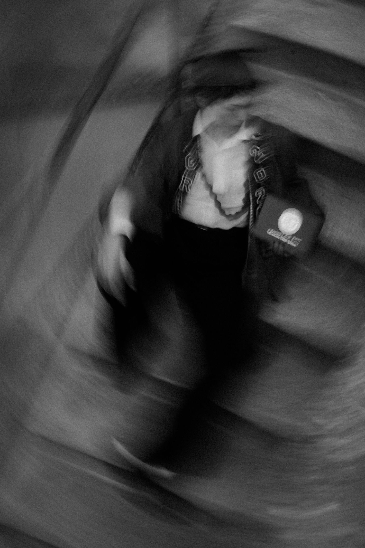 Blurred black and white photo of a person in motion, creating an abstract swirl effect with dramatic lighting.