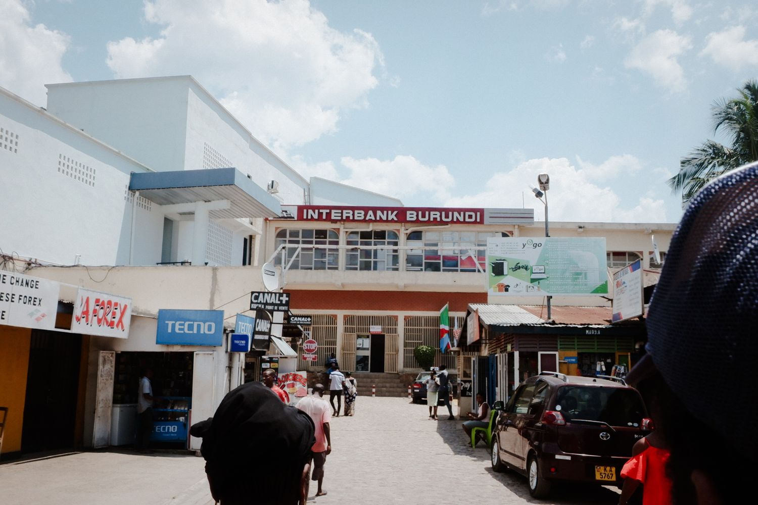 Strip mall exterior with white buildings and parked vehicles under blue sky.