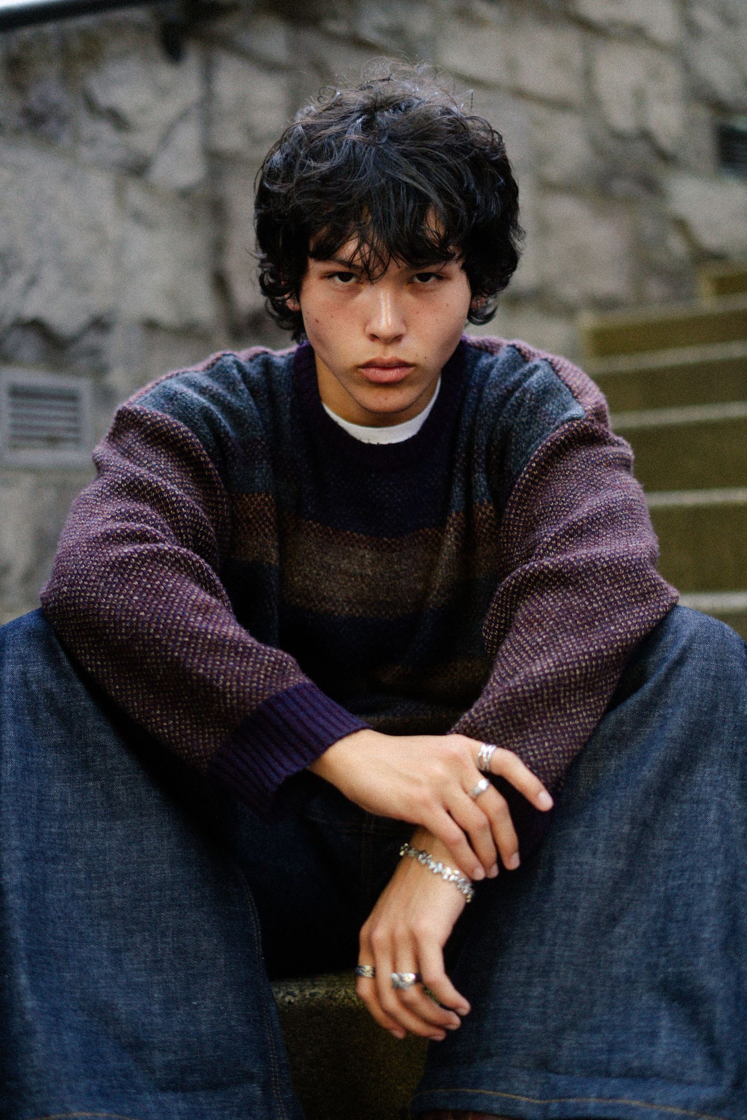 Moody portrait of person wearing knit sweater sitting on outdoor steps.