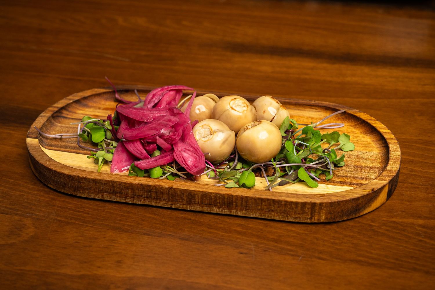 Wooden serving board with pickled red onions, small mushrooms, and fresh microgreens.