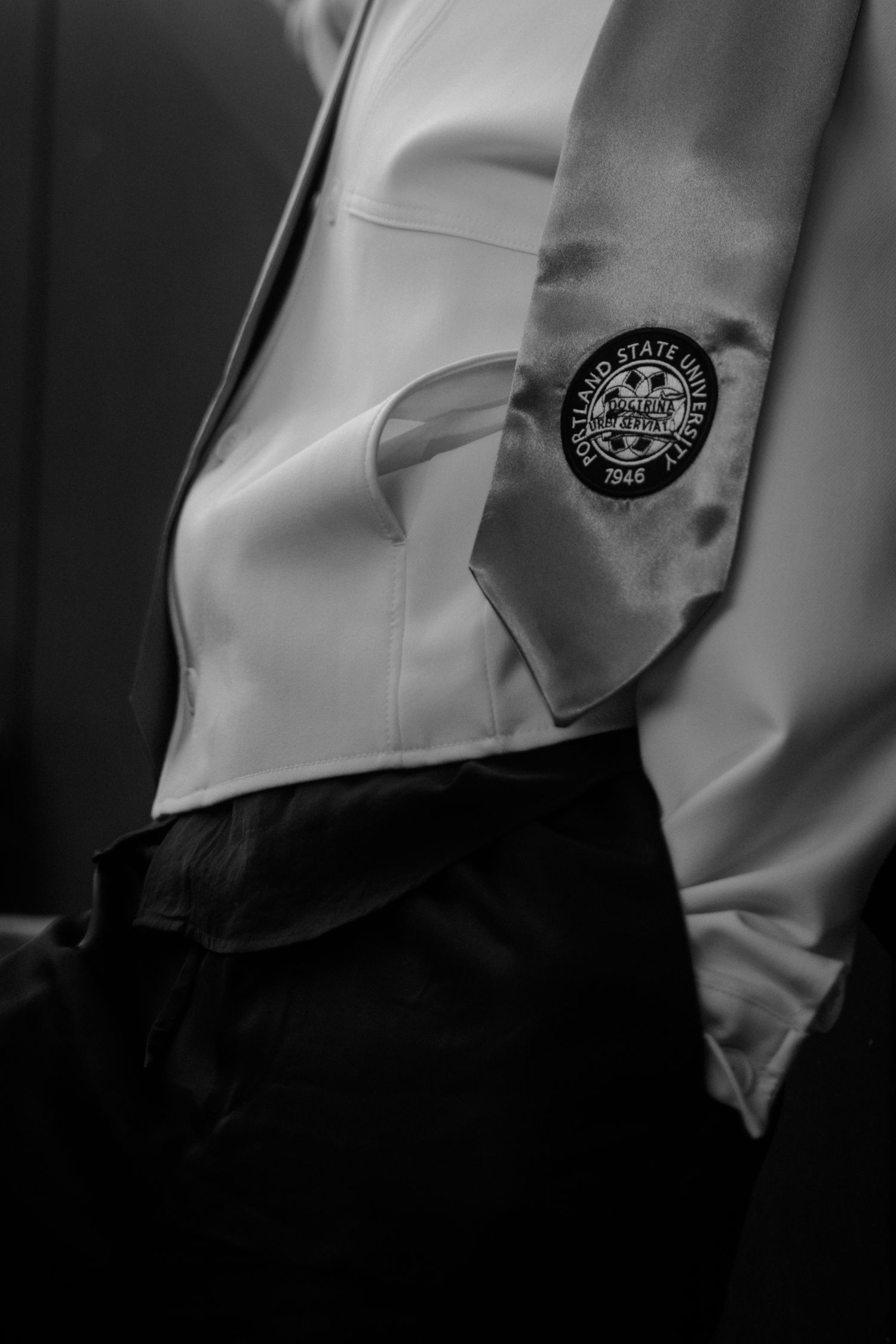 Black and white photo of Portland State University graduation regalia with embroidered seal on academic gown.