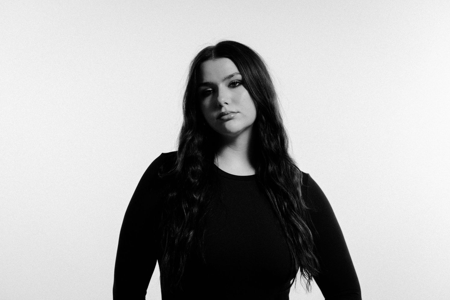 Black and white portrait of a young woman with long dark hair wearing a black top against a white background.
