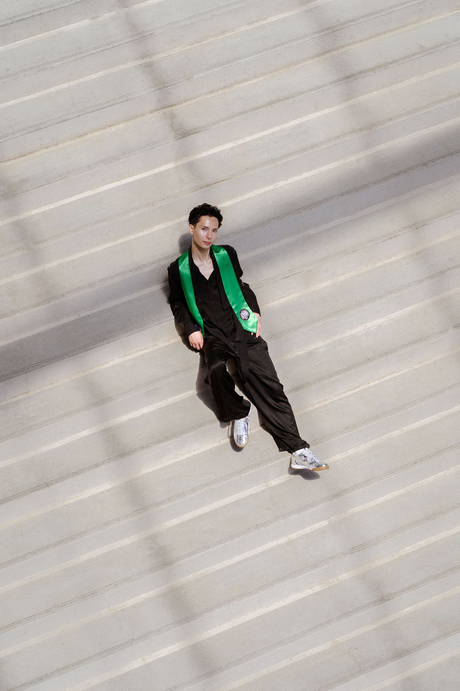 Young person in black outfit with green scarf poses on wide concrete steps, shot from above.