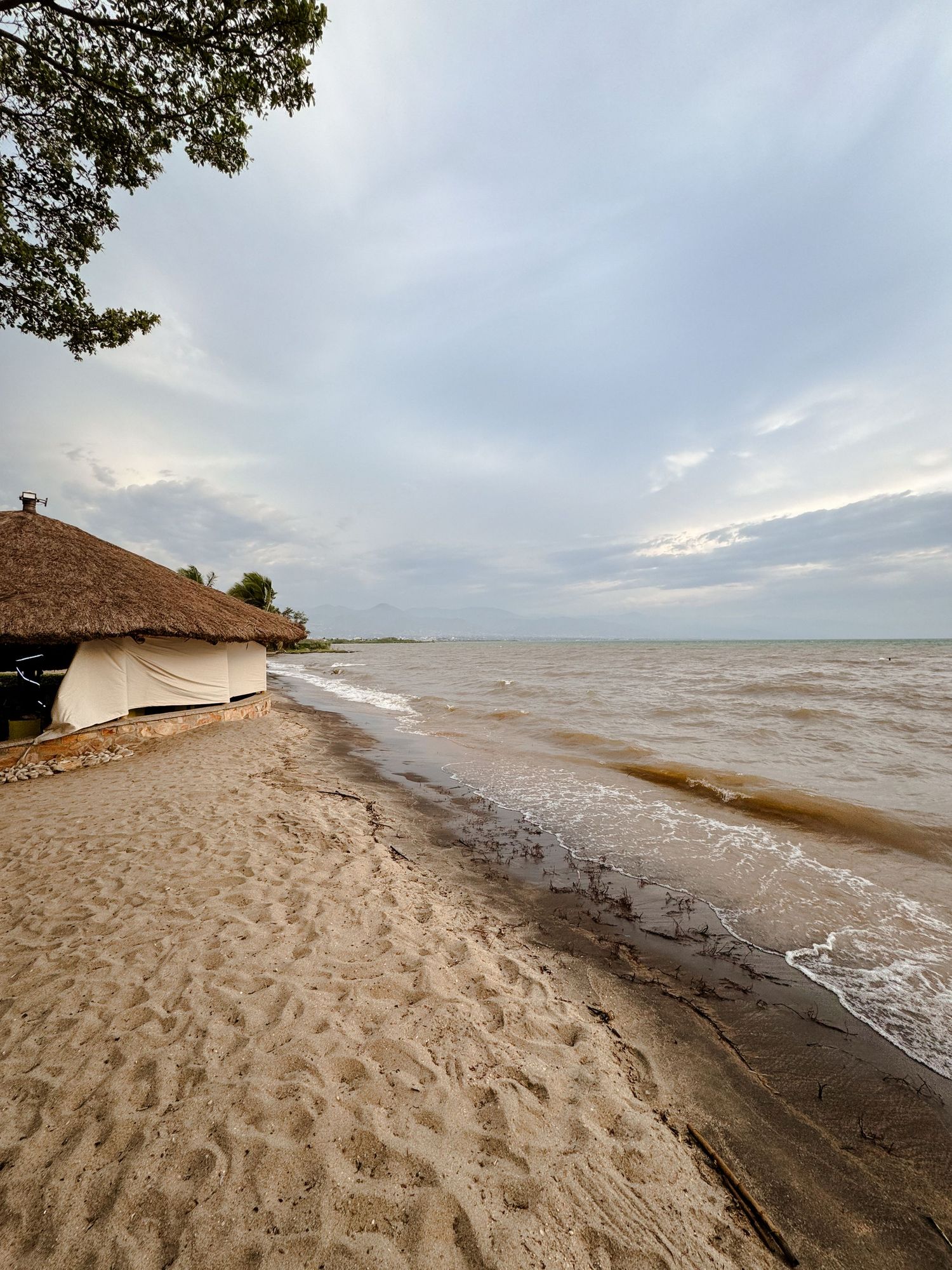 Sandy beach shoreline with waves meeting the coast under cloudy skies.