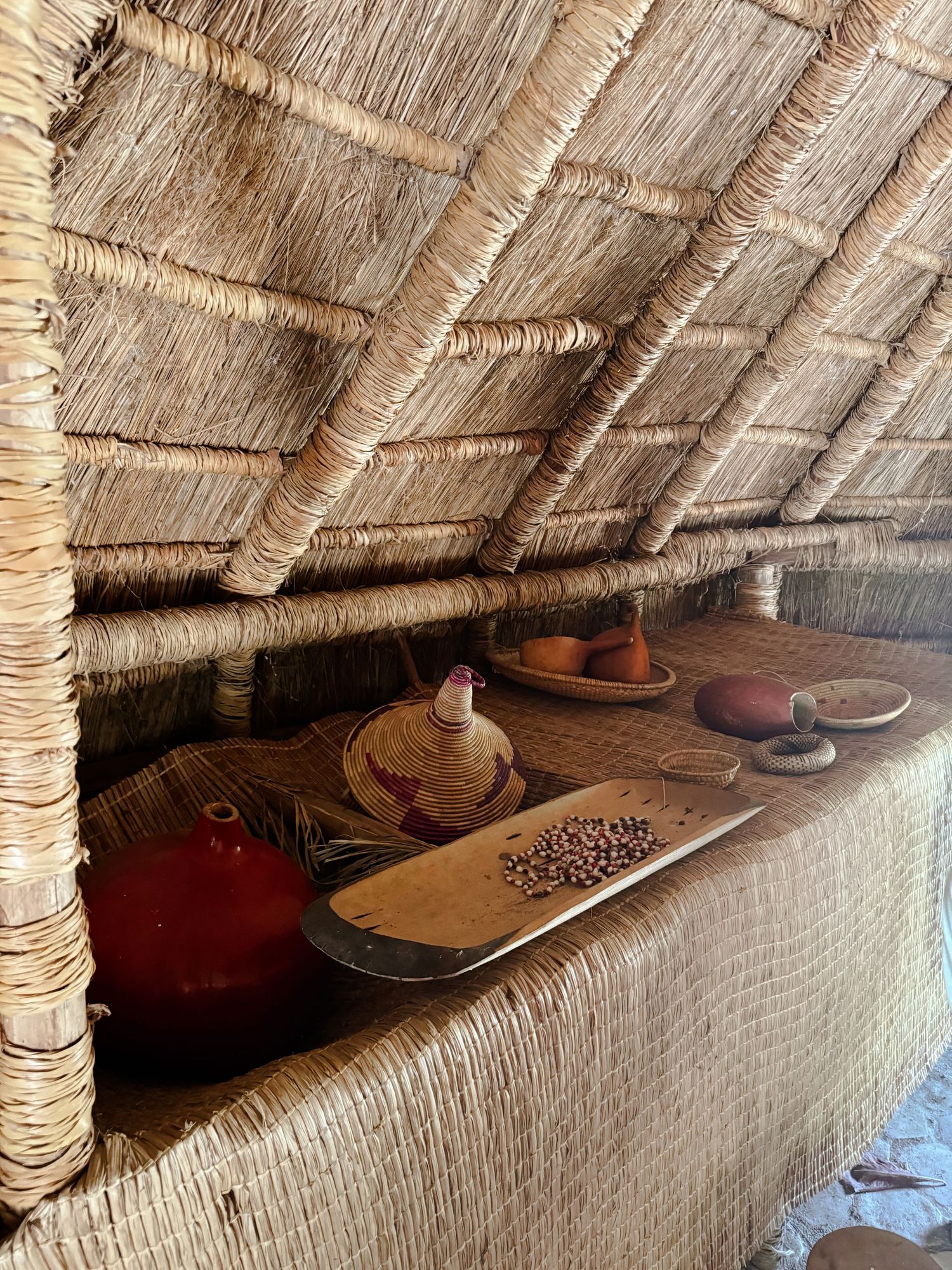 Traditional thatched roof interior with hats and personal items stored along wooden beams.