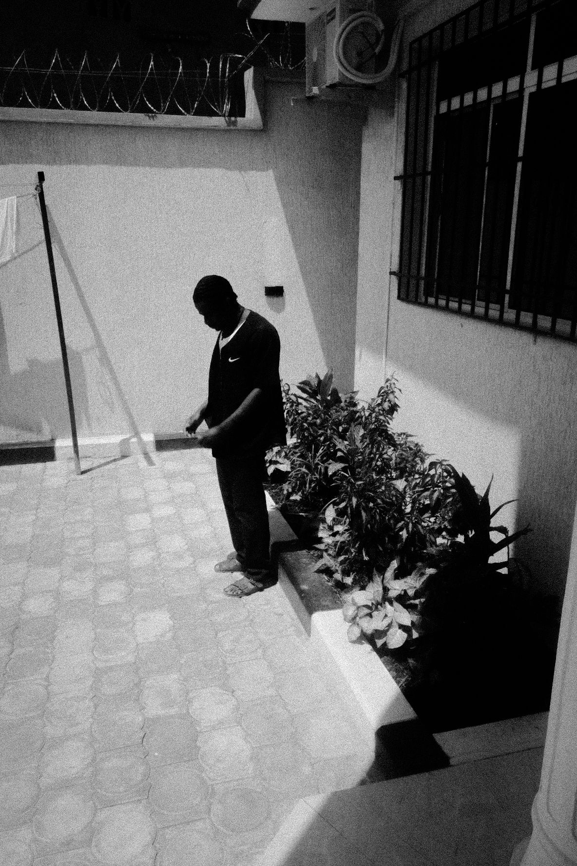 Black and white security camera footage showing a tiled walkway with potted plants.