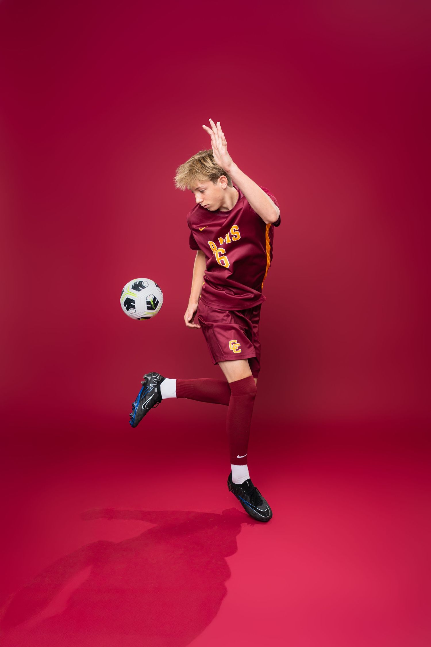 Soccer player demonstrates ball control moves against red studio backdrop.